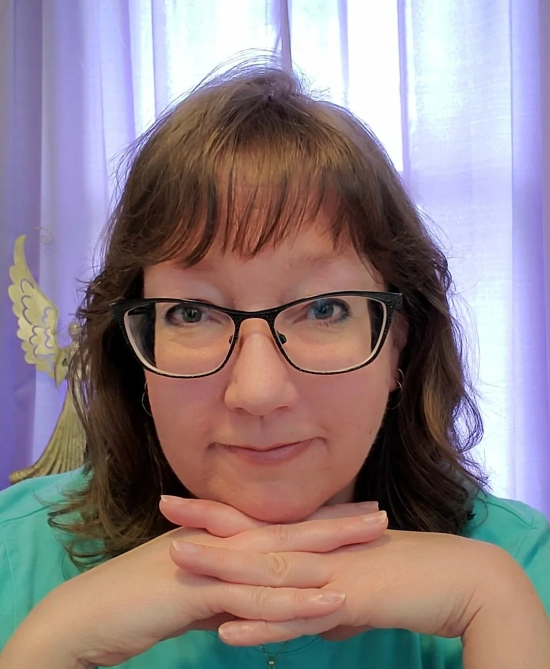 A woman with glasses resting her chin on her hands, with a purple curtain and a decorative gold eagle emblem in the background.