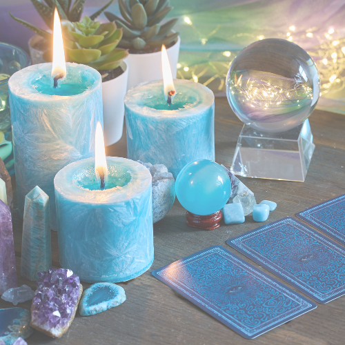 A table with three lit blue candles, crystal and stone objects, a crystal ball, and tarot cards.