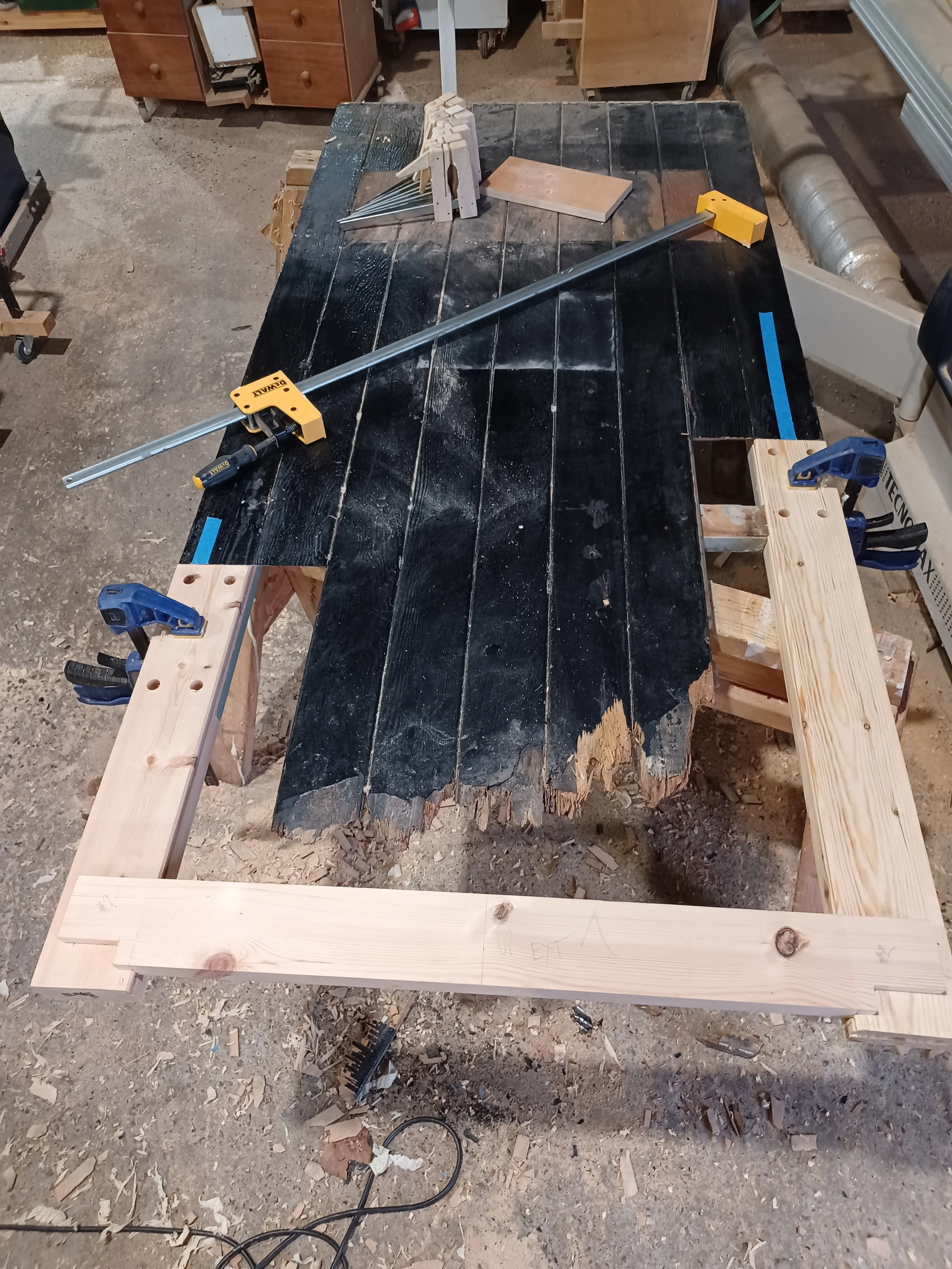 Workshop table with woodworking tools and clamps around a large, partially sanded black wooden slab.