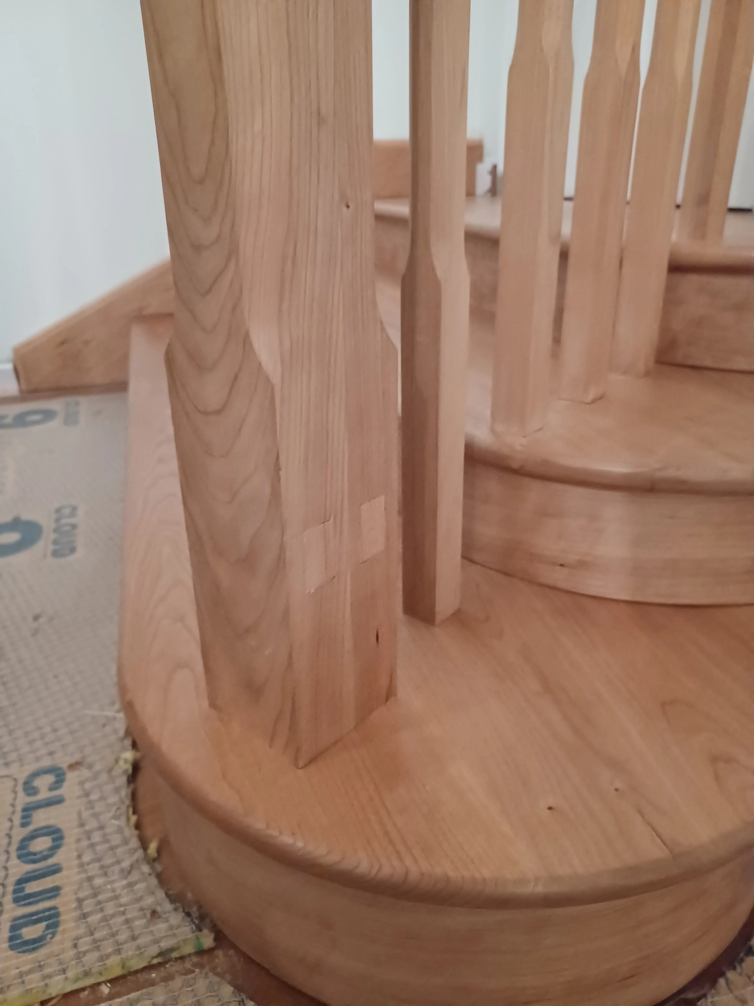 Close-up of a wooden staircase with spindles and a curved base, showing the wood grain and construction details.