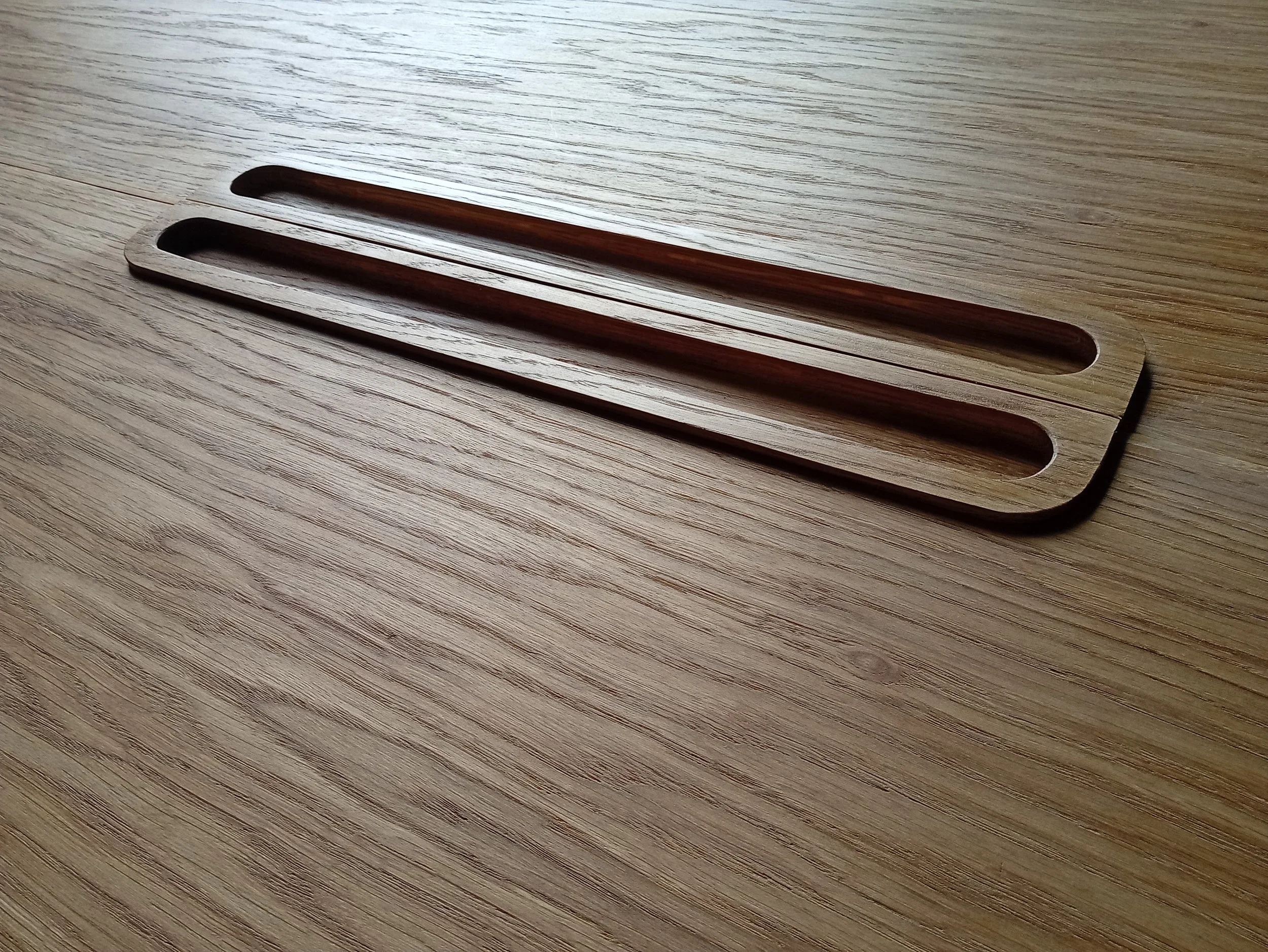 Wooden utensil with two elongated slots on a light wood table.