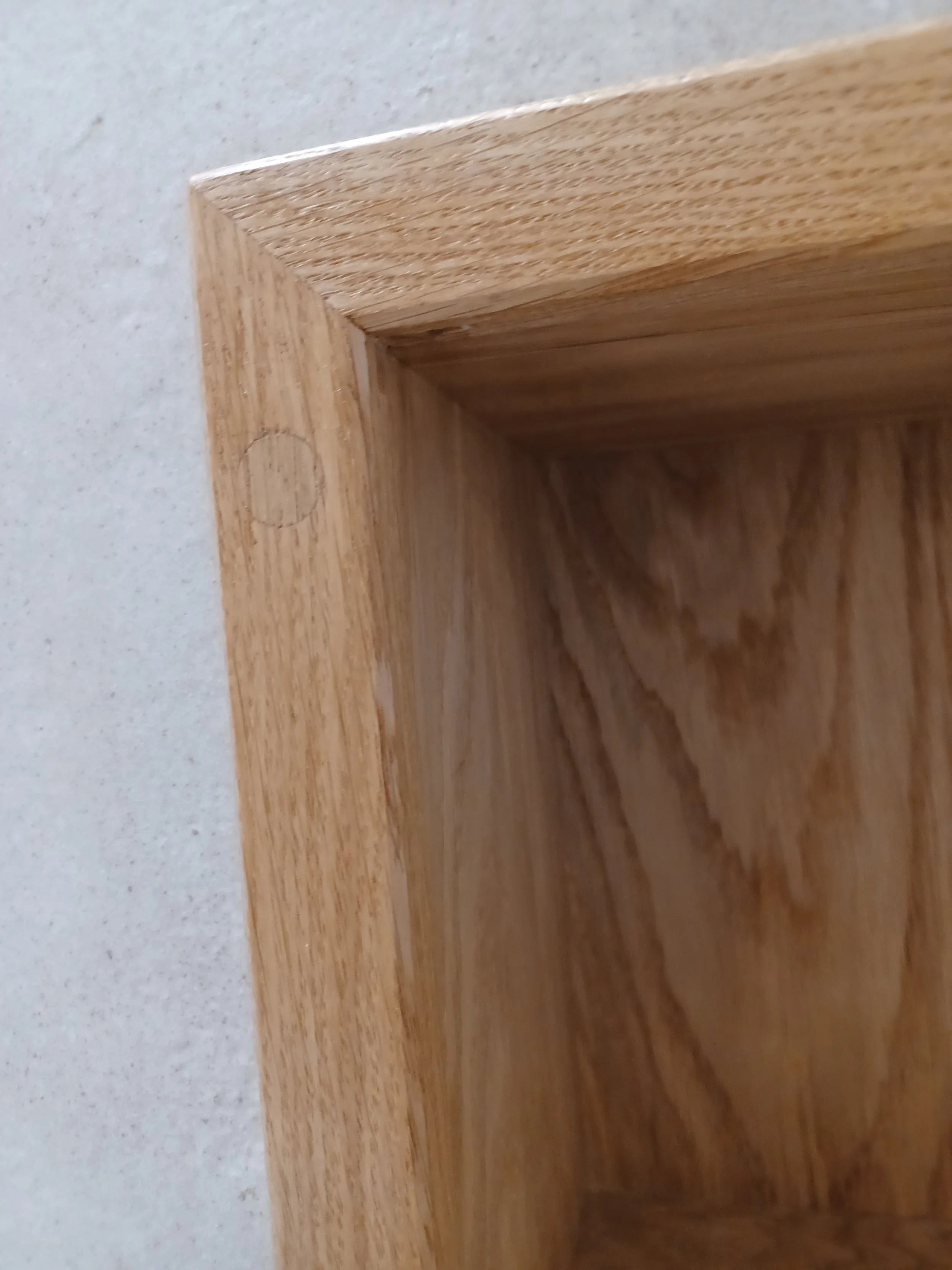 Close-up of the corner of a wooden frame or piece, showing the miter joint and a small circular indentation.