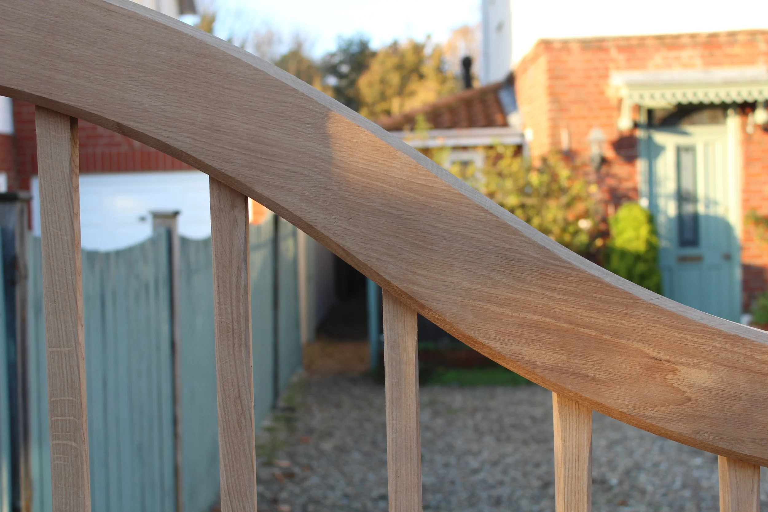 Close-up image of a wooden handrail on a staircase with a blurred background of a residential neighborhood.