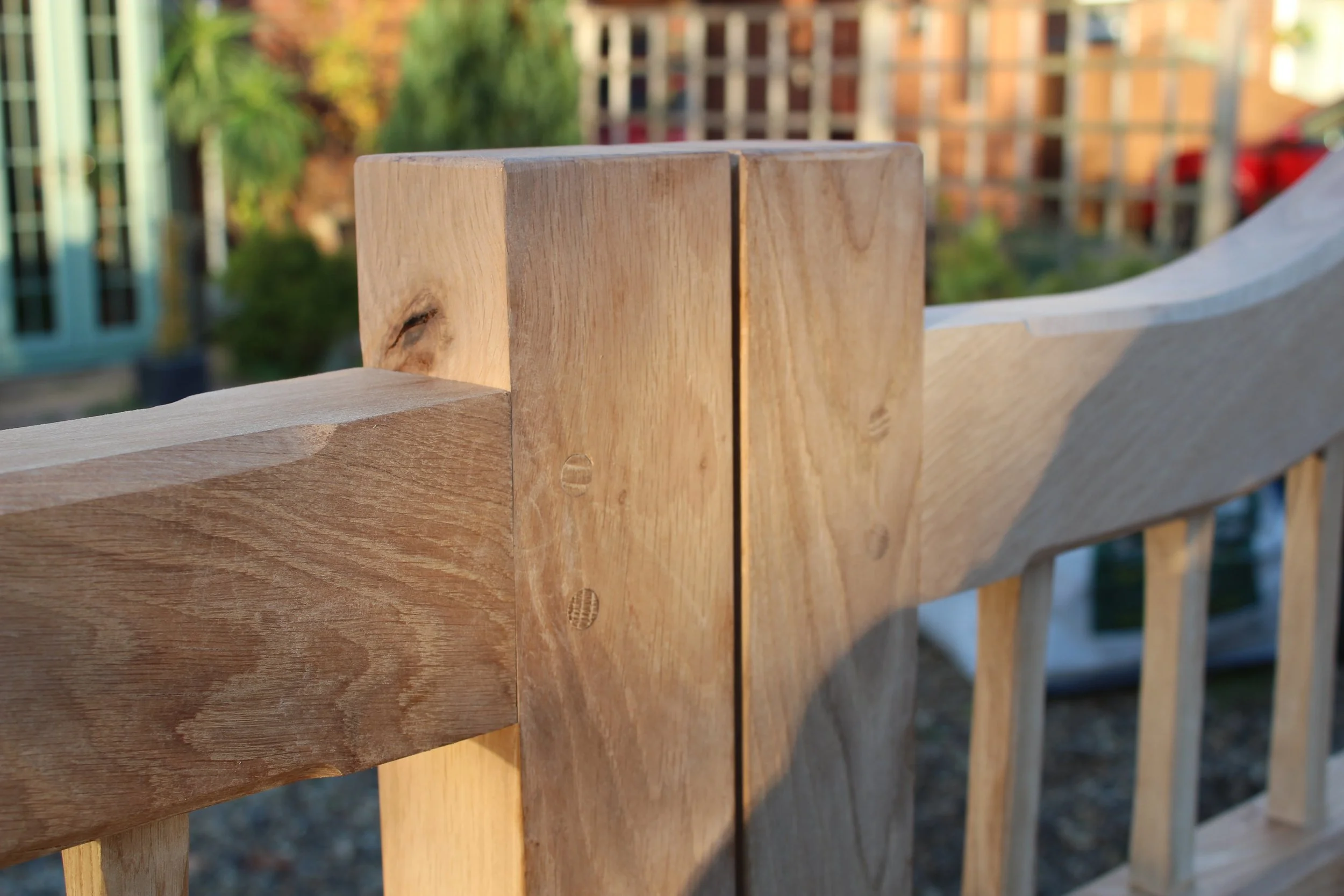 Close-up of a wooden fence with vertical and horizontal planks, showing nails and wood grain, outdoors with blurred trees and buildings in the background.