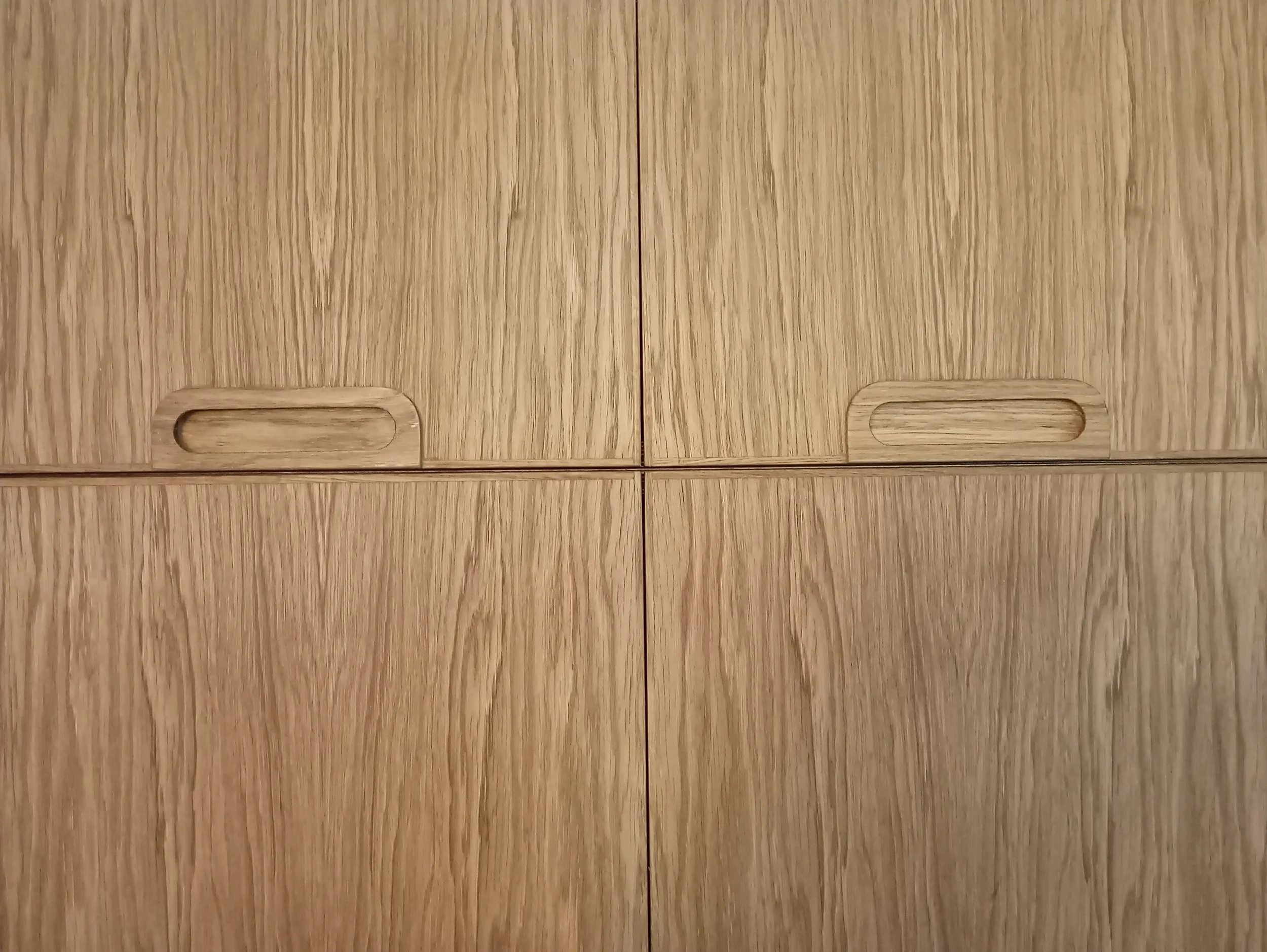 Close-up of a wooden cabinet door with integrated handle cutouts.