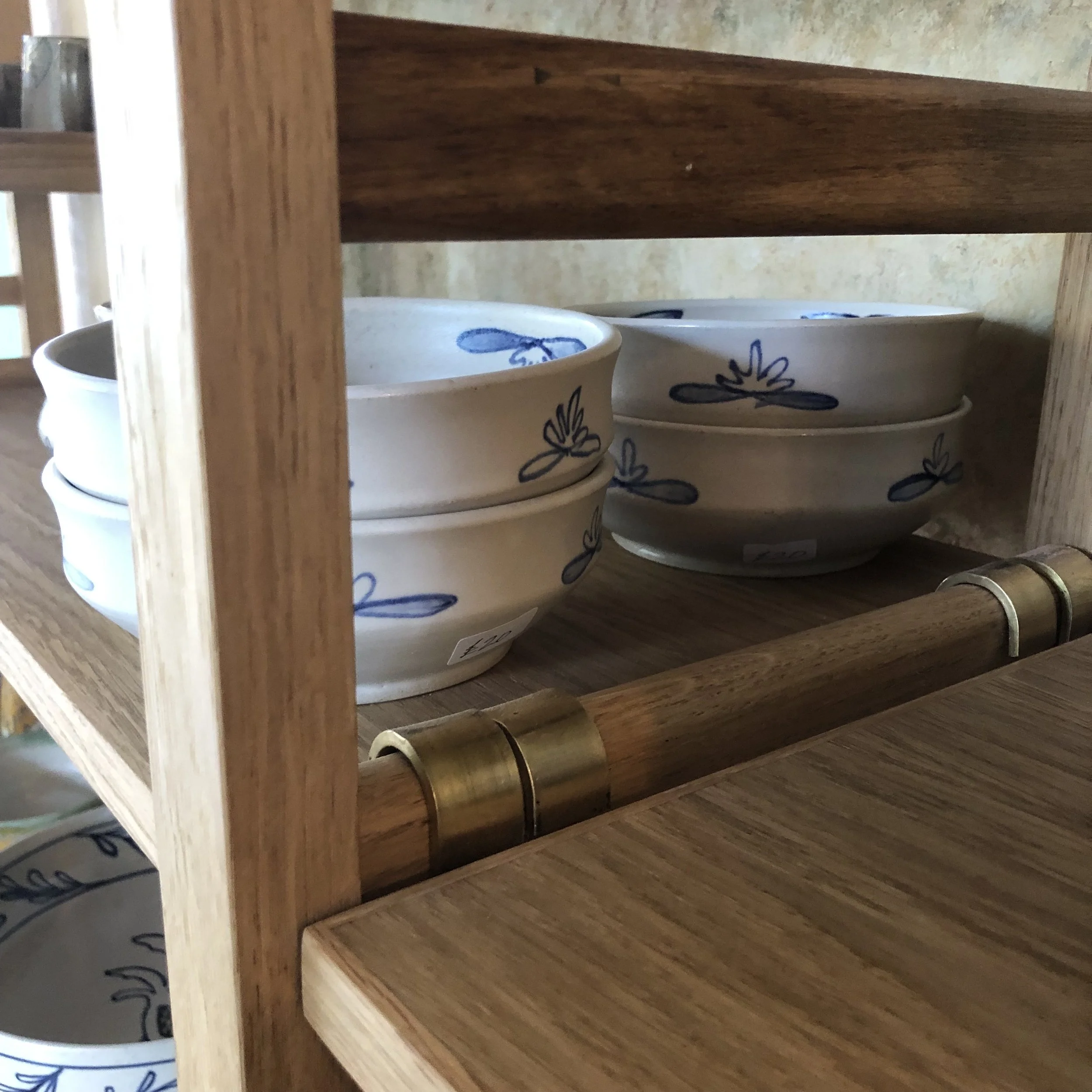 Stacked white ceramic bowls with blue floral patterns on a wooden shelf with brass accents.