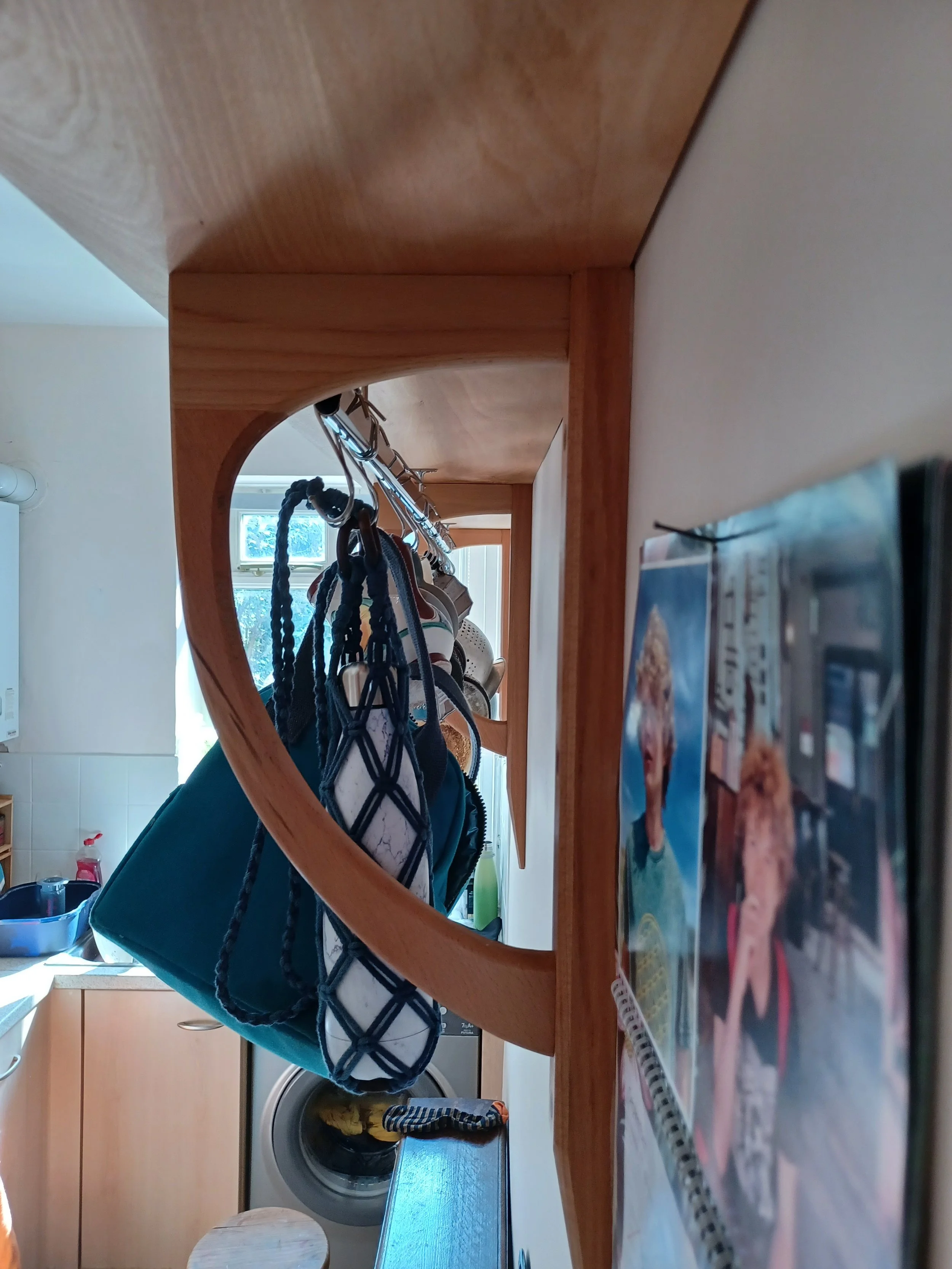 A view of a kitchen with wooden shelves hanging on a wall, holding bags and various items, with a photo of a child and a woman on the right side, and a washing machine below a window in the background.