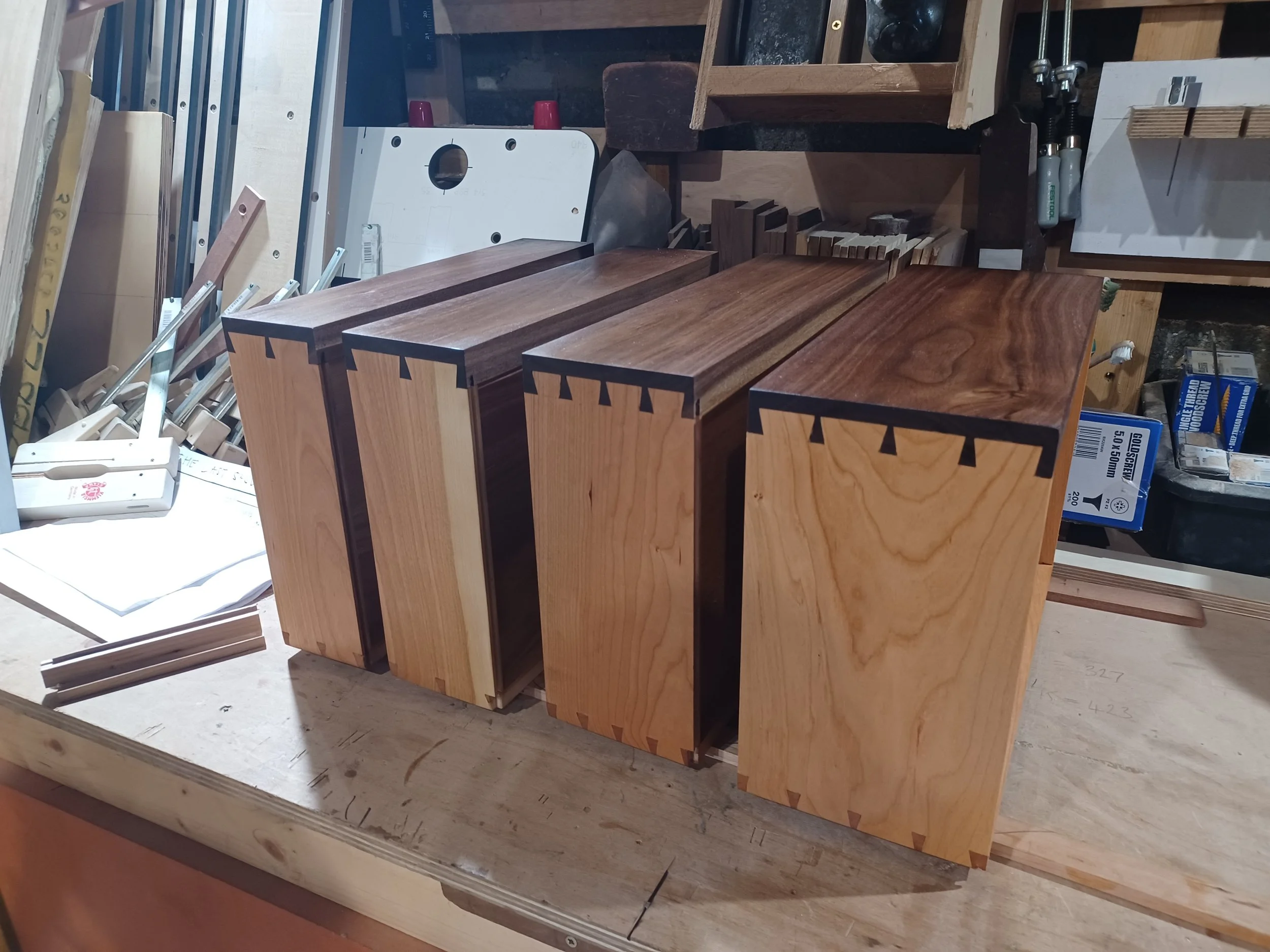 Four wooden boxes with dovetail joints on the corners arranged on a workbench in a woodworking shop.