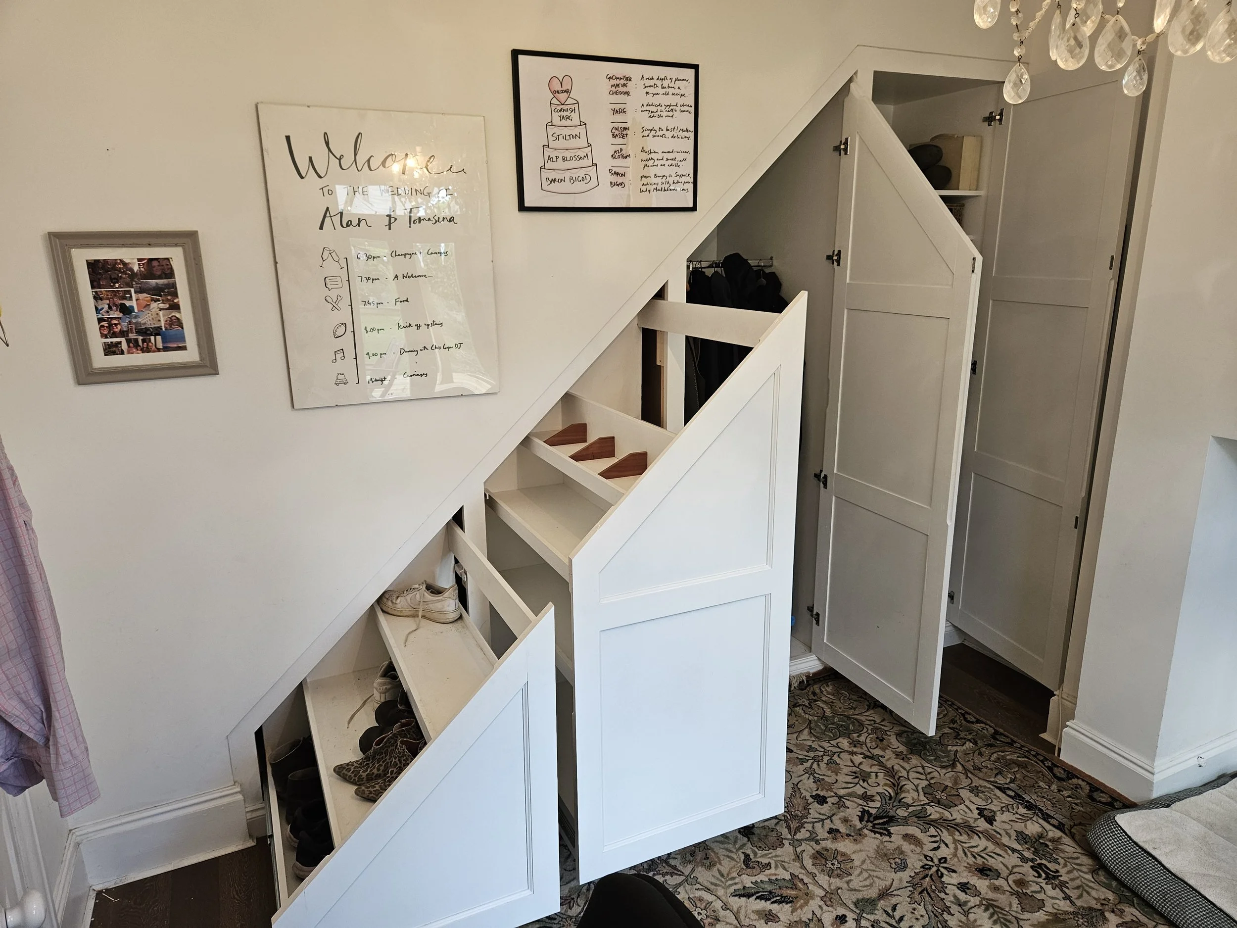 White built-in shoe storage with cubbies and cabinets under a sloped ceiling in an entryway, with decorative wall art and a patterned area rug.