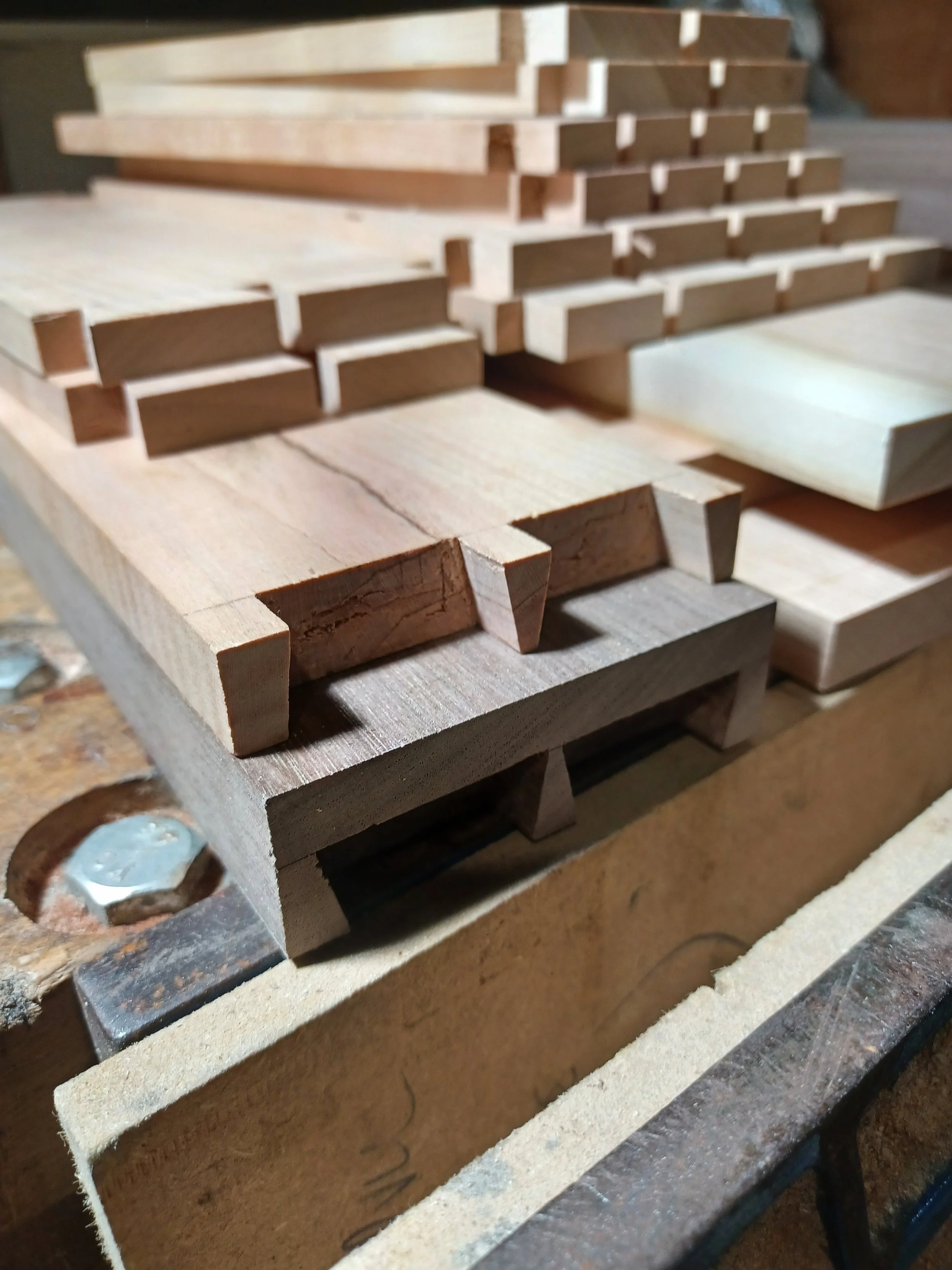 Close-up of interconnected wooden pieces on a workbench, some with angled cuts, used for woodworking or carpentry.