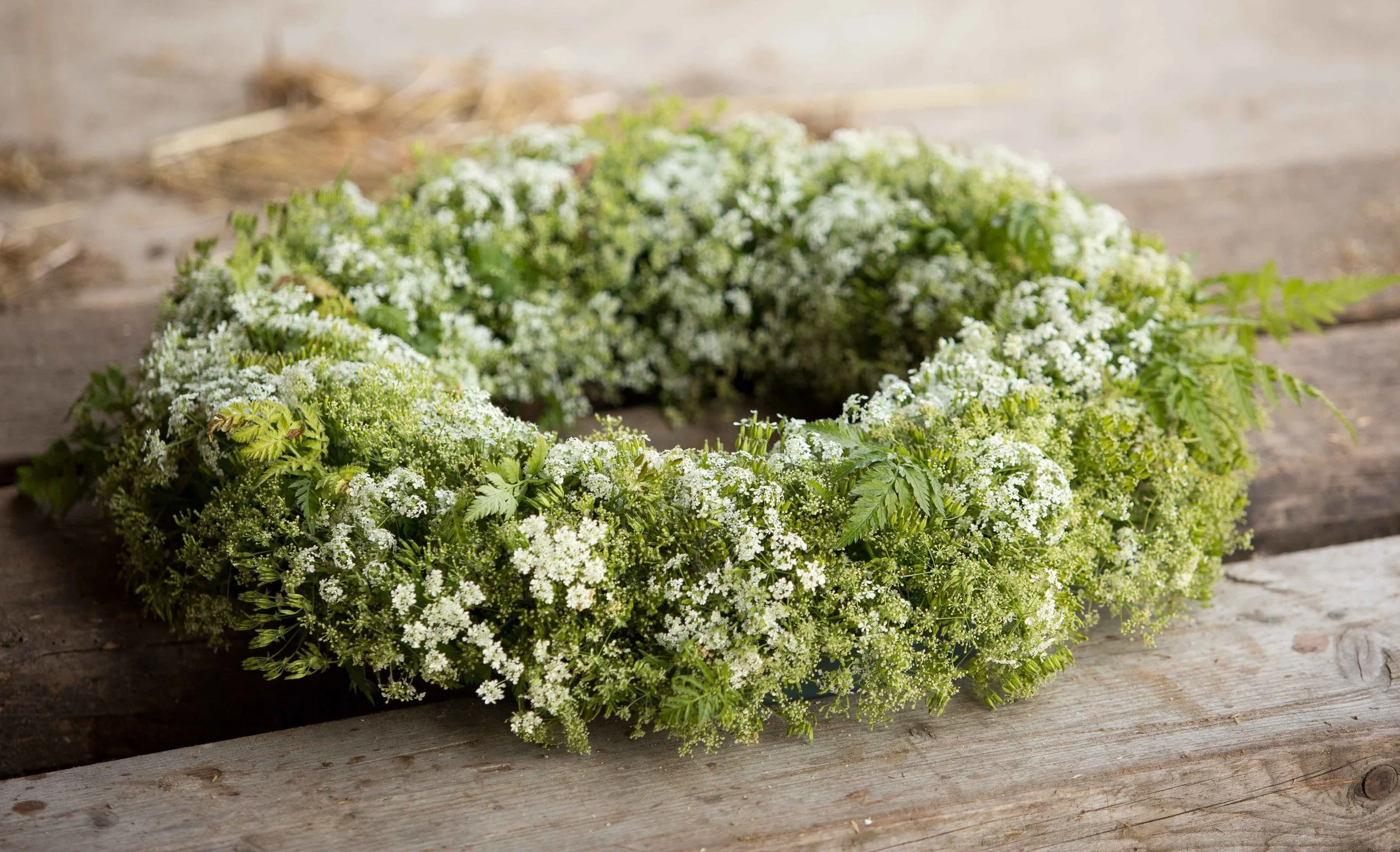 Een bloemenkrans gemaakt van kleine witte bloemen en groene bladeren, ligt op een houten tafel.