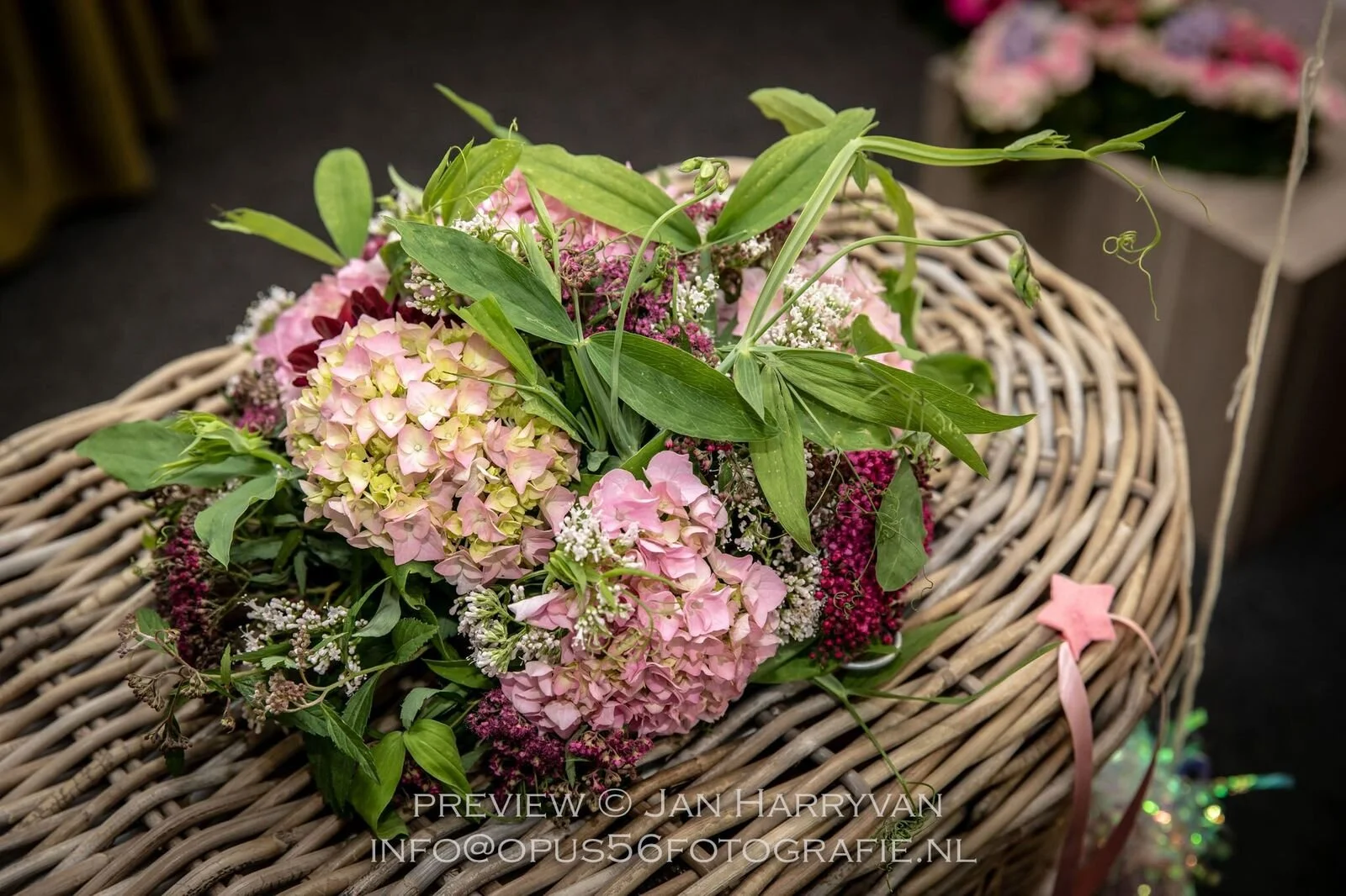 Een bloemenarrangement met roze en witte hortensia's en groene bladeren, geplaatst in een rieten mand.