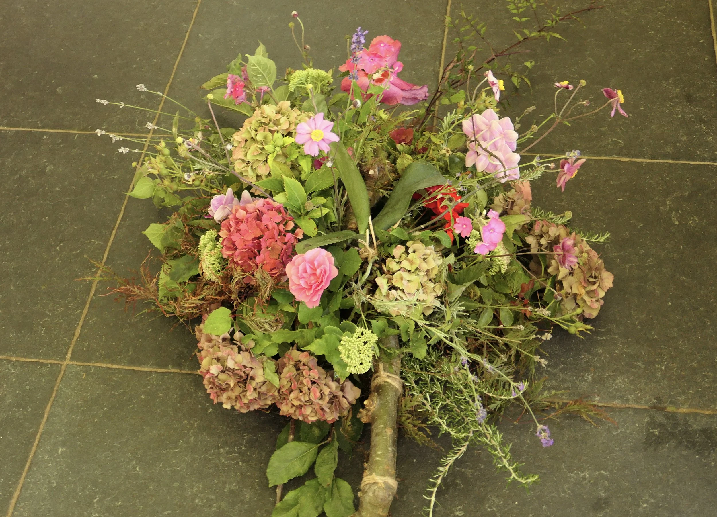 Een bos bloemen met verschillende bloemen en groen, gelegd op een tegelvloer.