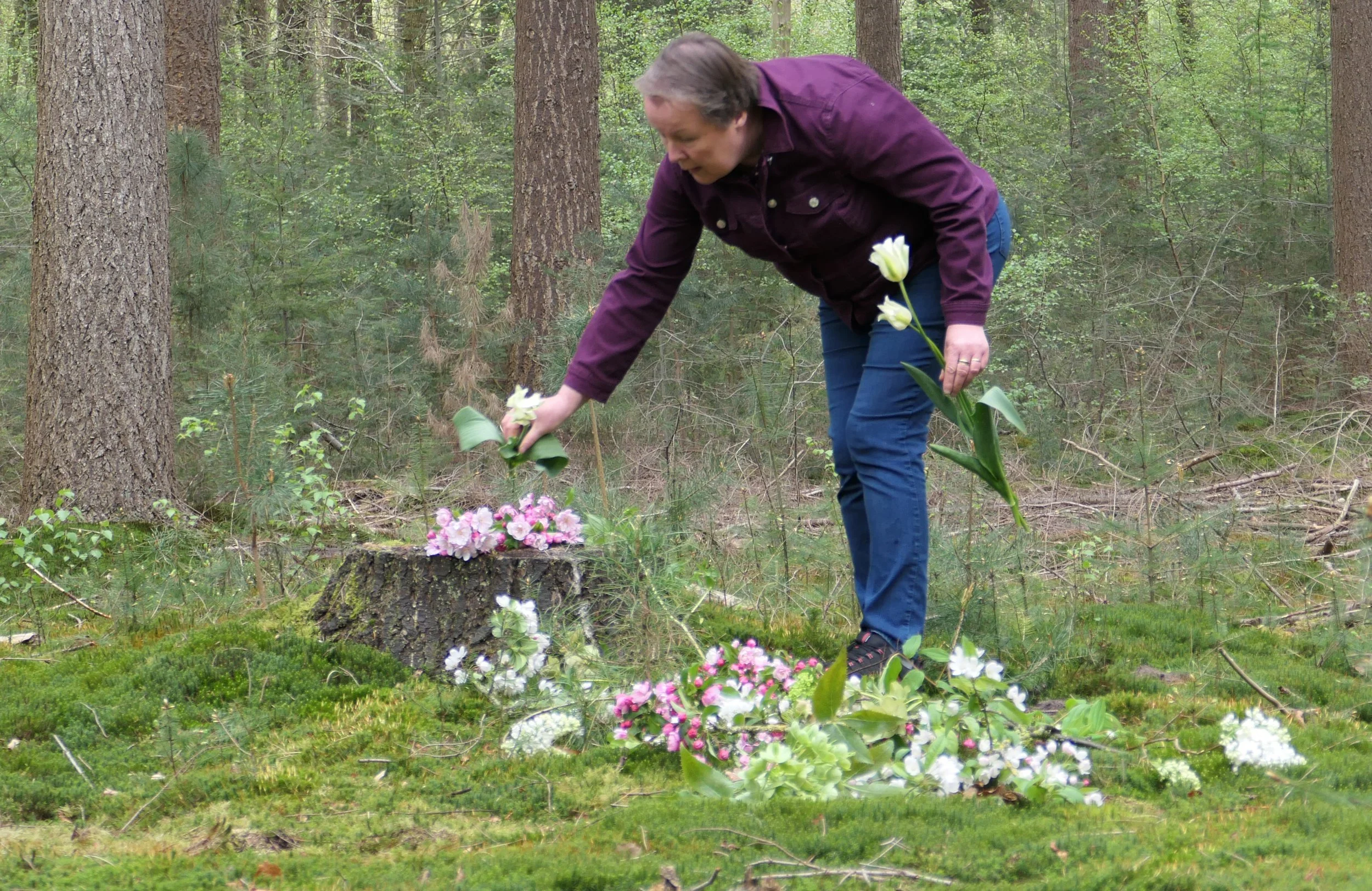 Vrouw legt bloemen neer op een boomstam in een bos.