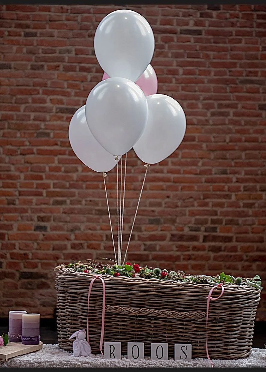 Mand van hout met bloemen en decoraties, omringd door witte en roze ballonnen, met de letters R O O S in blokletters.