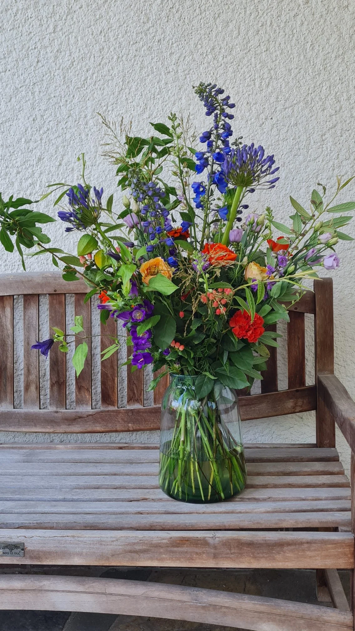 Een bloemenvaas met een kleurrijk boeket op een houten tuinbank.