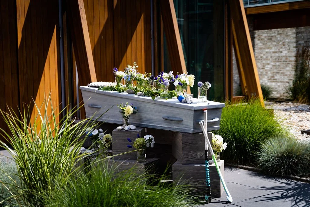 Een graf met bloemen, gelegen in een tuin met groene planten en een houten muur op de achtergrond.