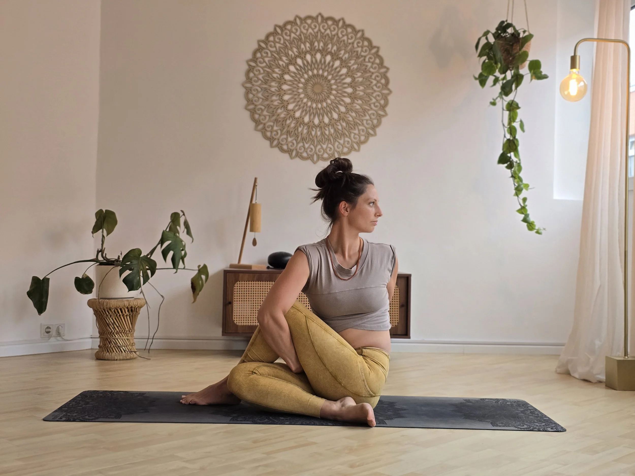 Eine Frau macht Yoga auf einer schwarzen Matte in einem hell eingerichteten Raum mit Pflanzen und dekorativen Elementen.
