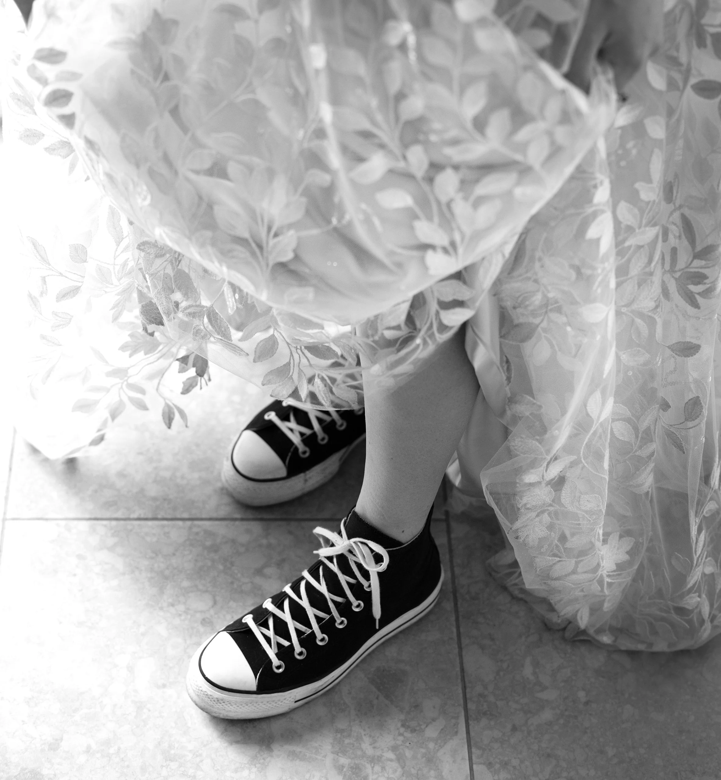 Black high-top converse with white laces and soles, worn by a person whose legs are visible, under a wedding dress