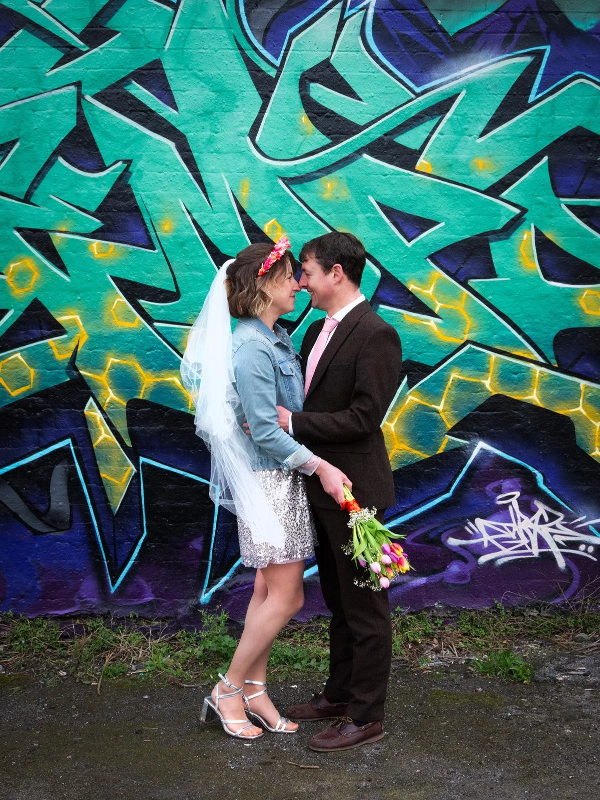 Alternative bride and groom kissing in front of colourful graffiti wall during creative wedding portraits.