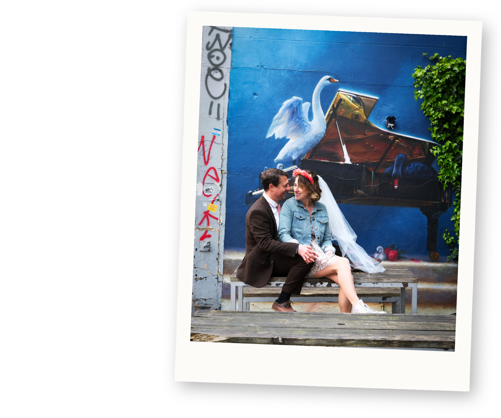 Alternative bride and groom sitting together in front of colourful street art during a relaxed wedding portrait in Bristol