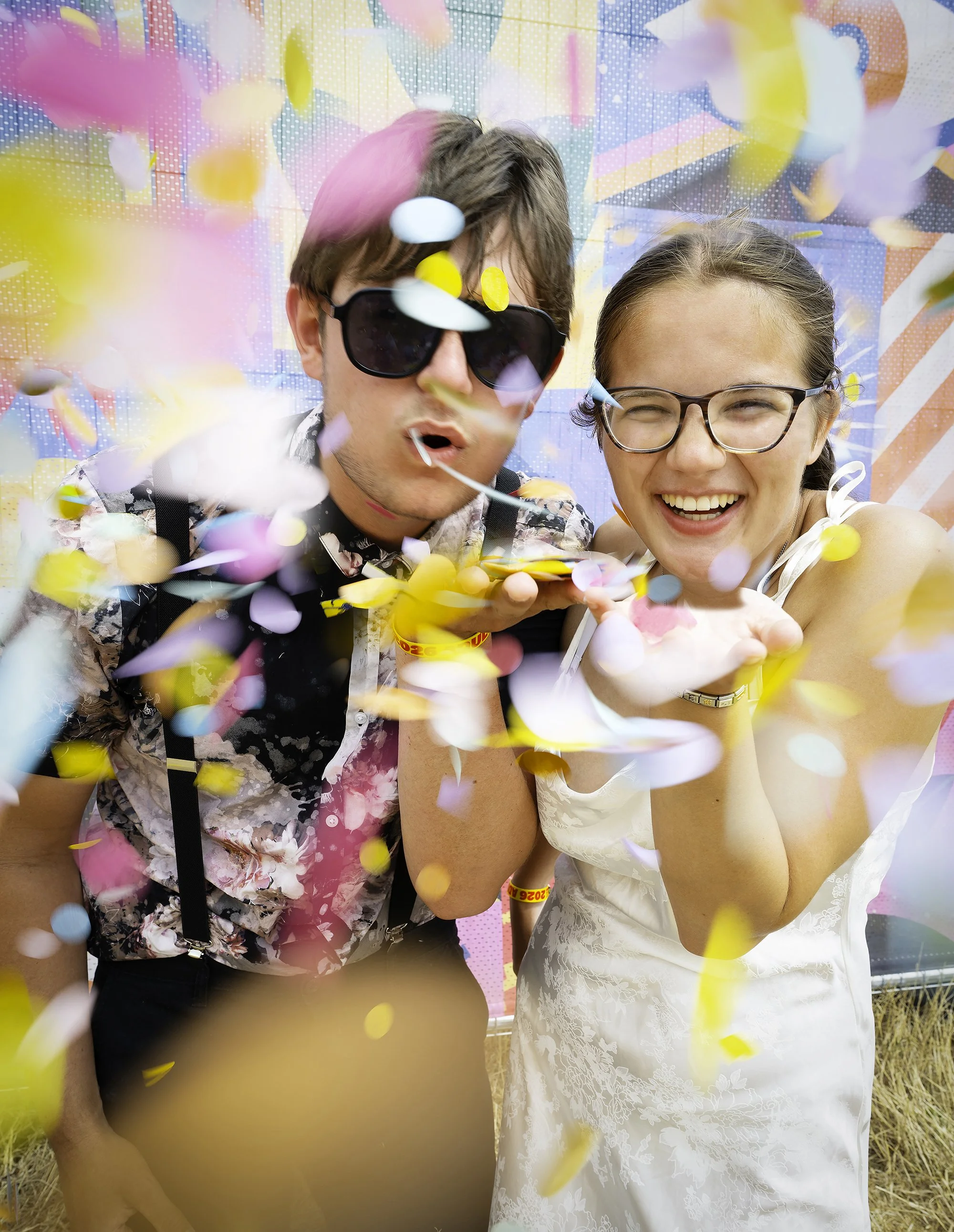 Bride and groom laughing as colourful confetti flies towards the camera.