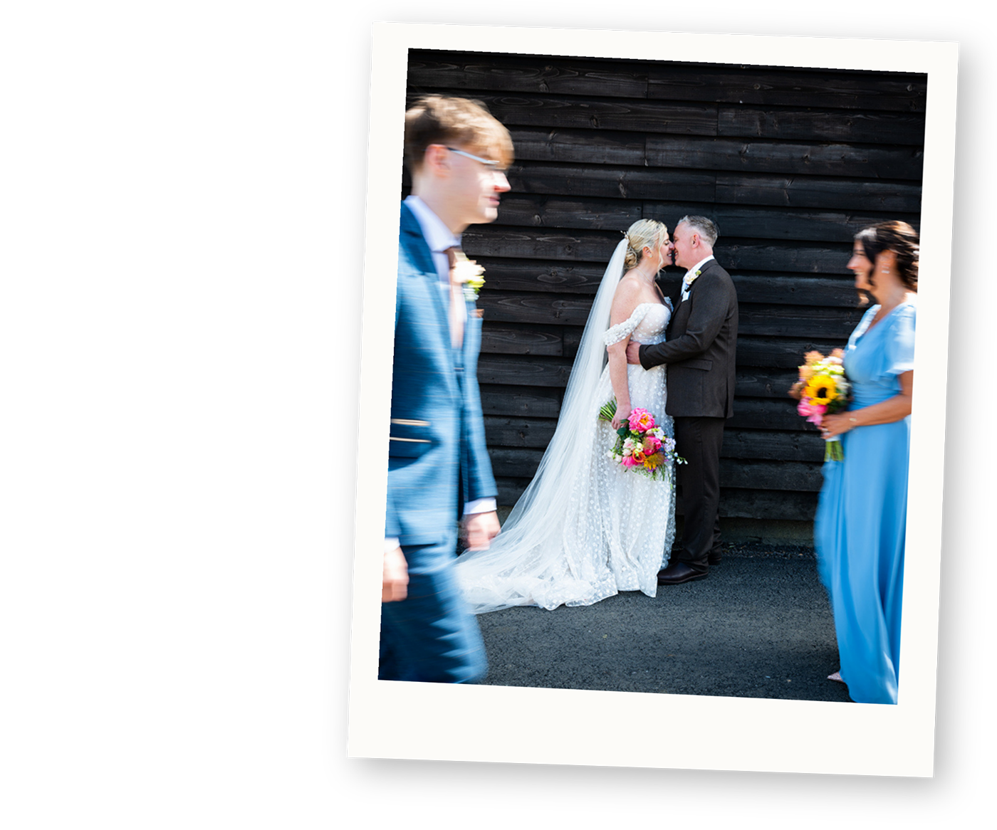Bride and groom sharing a kiss while guests walk past during a colourful alternative wedding.