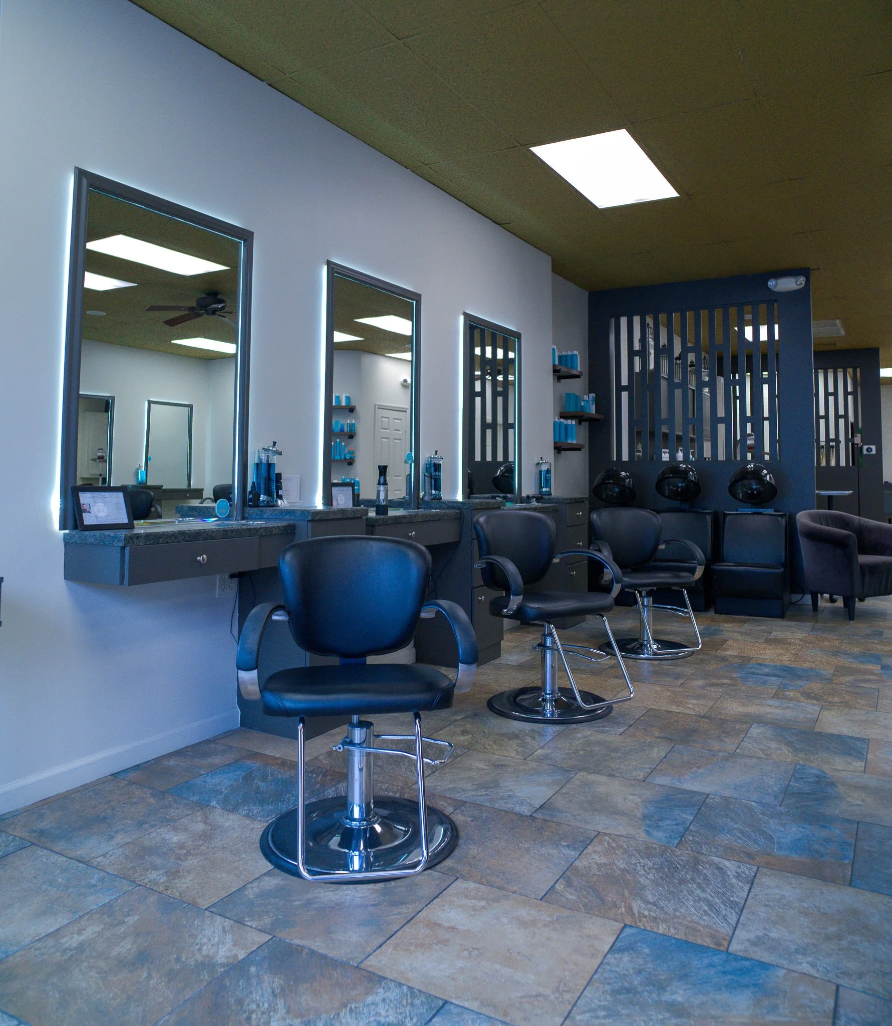 Welcoming waiting area at Willow's Cove Salon featuring a velvet accent chair, large tropical plant, and stone column in Mineola, NY