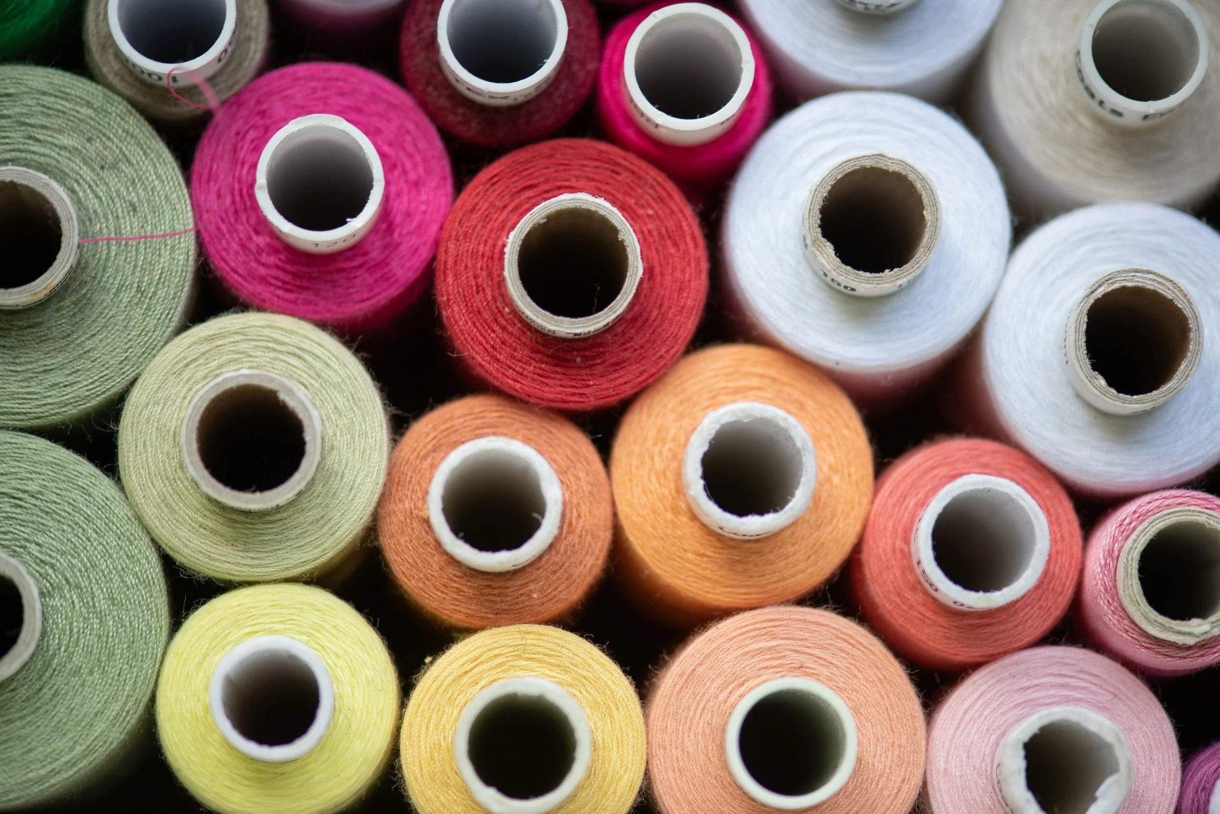 Spools of colorful thread arranged closely, including pink, white, green, yellow, orange, and red, representing the textile industry.