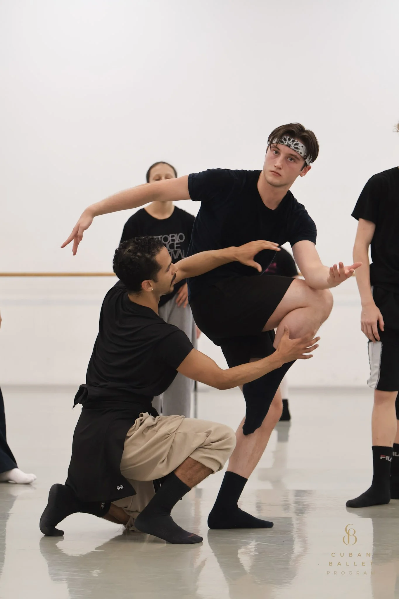 Dancer balancing on one leg with assistance from instructor in a dance studio