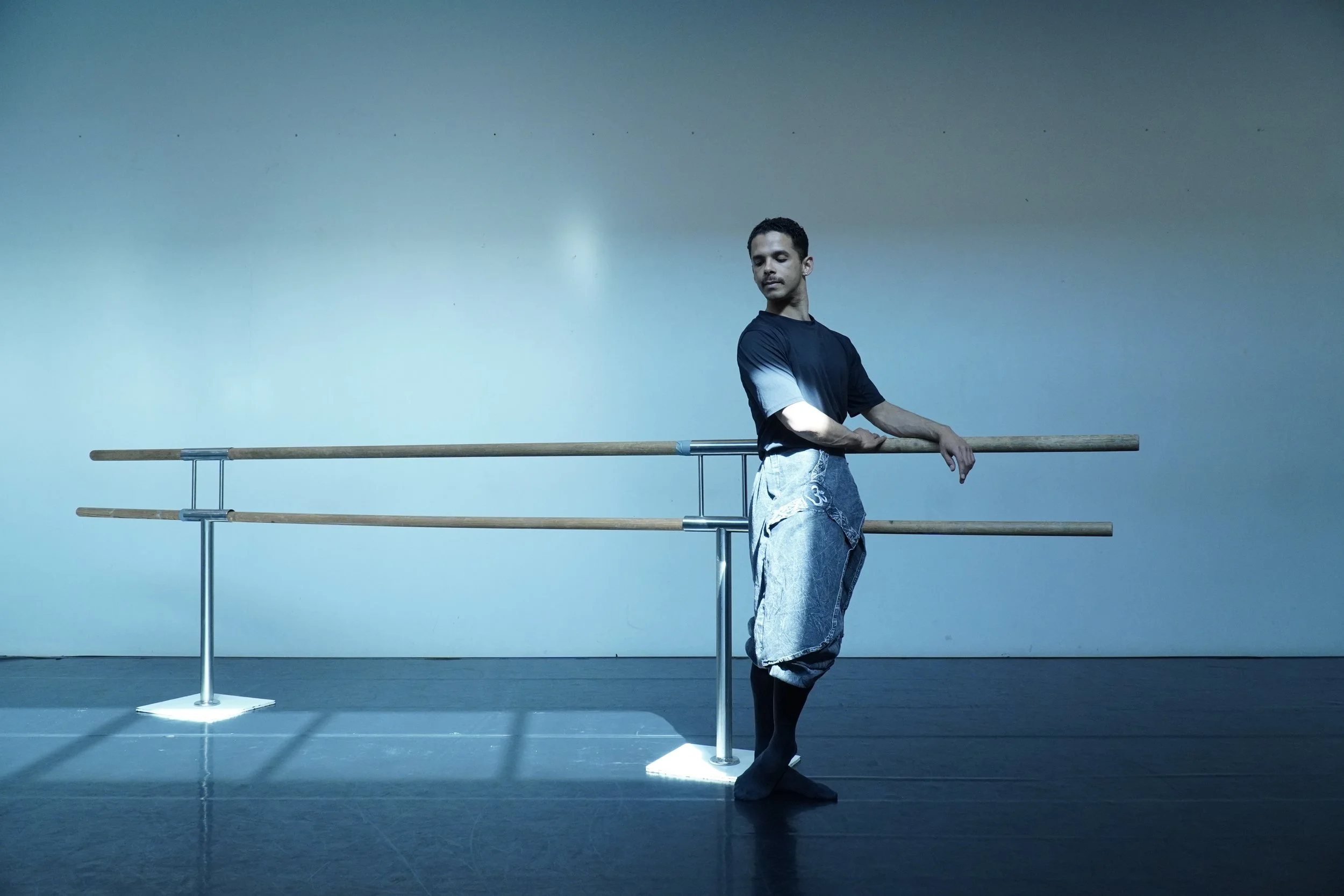 A man practicing ballet at a barre in a dance studio.