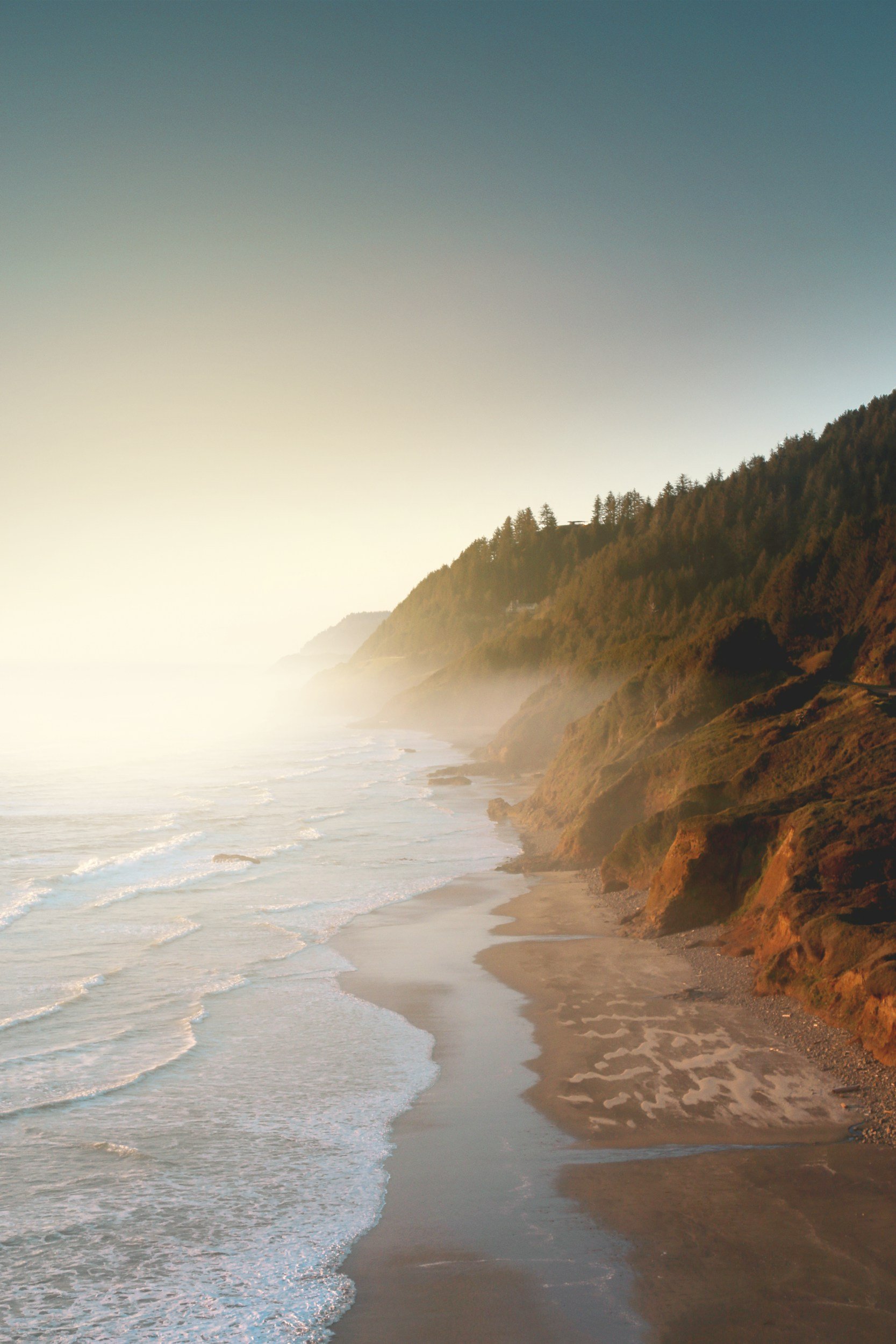 Warm photo of misty ocean waves and orange cliffs with trees in Oregon