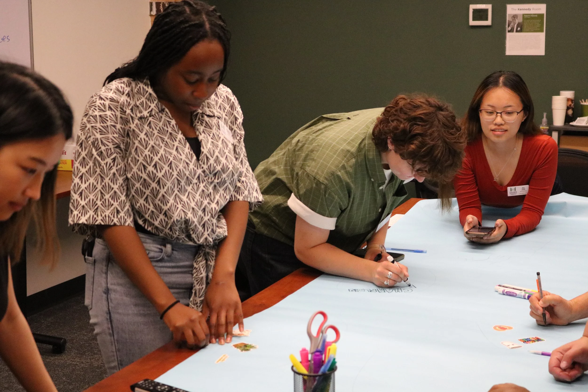Two women sitting at a table, smiling and laughing, engaging in a lively conversation, with papers, a water bottle, and a coffee cup on the table.