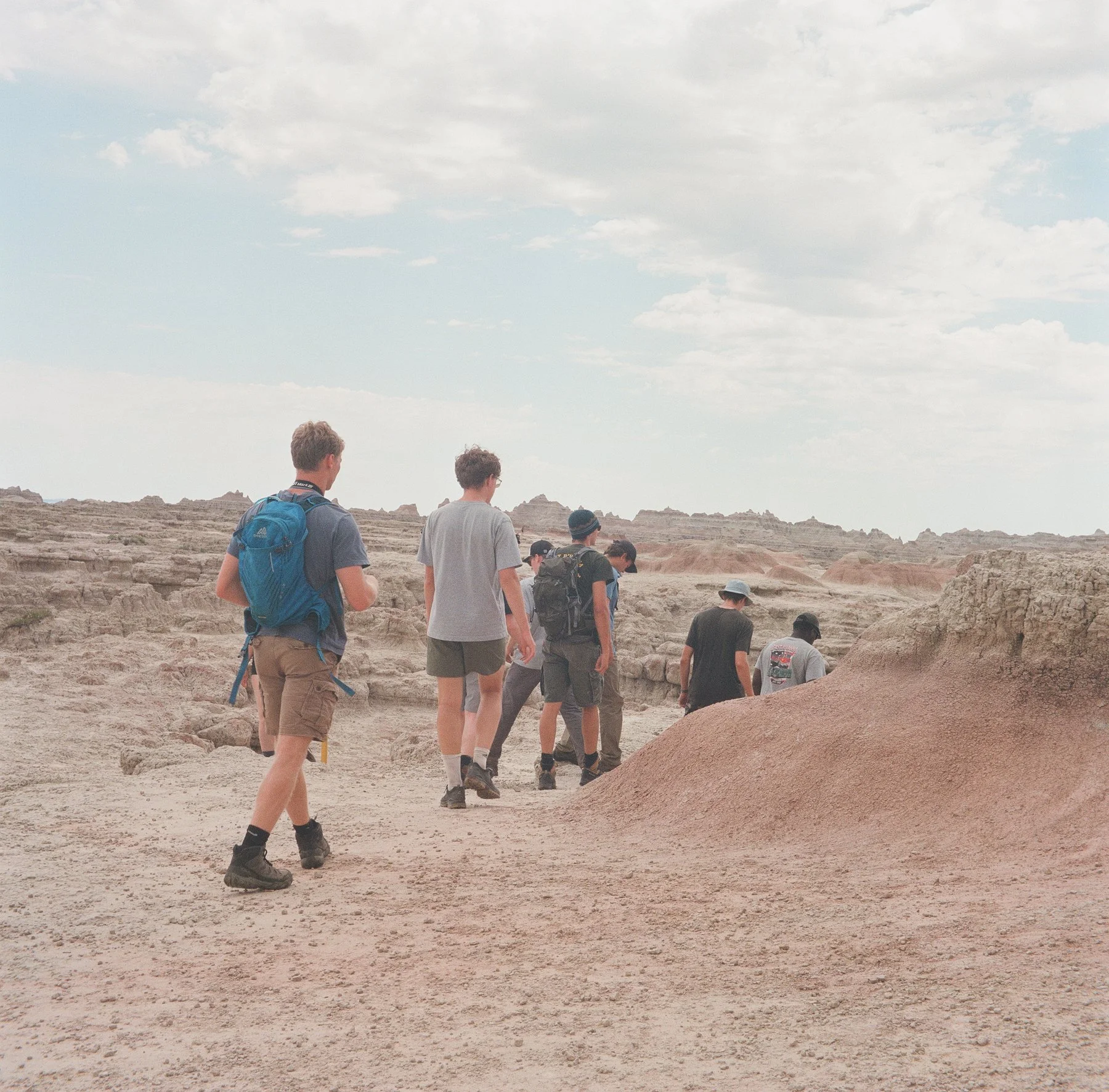 Group of hikers walking in a desert landscape under a partly cloudy sky.