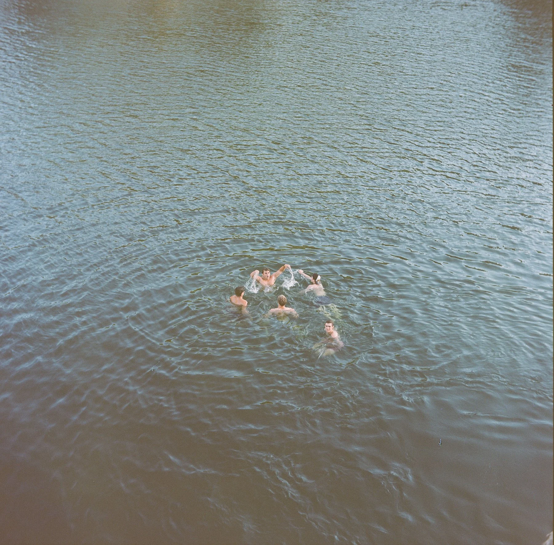 Five people swimming and playing in a large body of water on a sunny day.