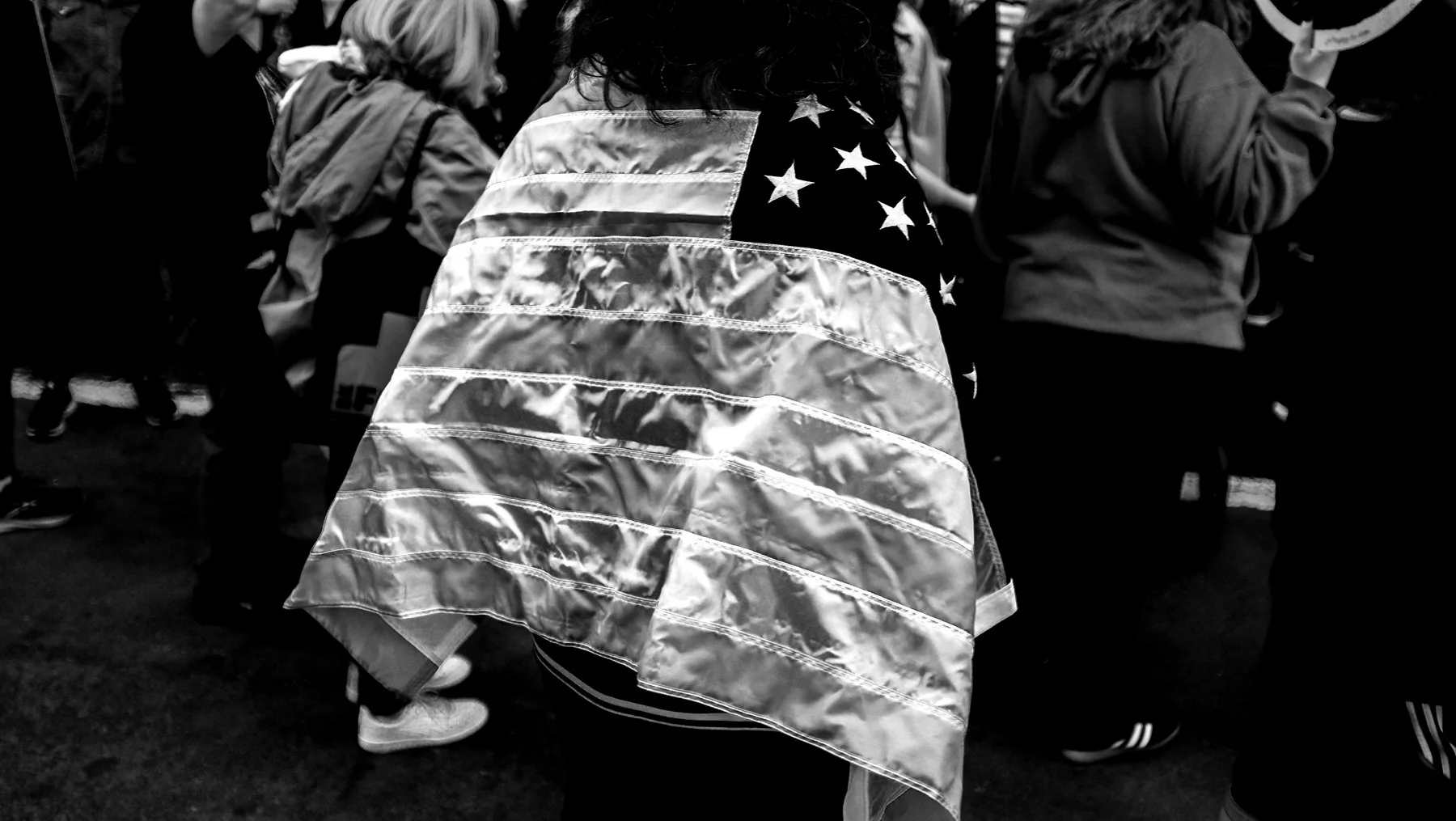 Person draped in a reflective American flag blanket in a crowd.