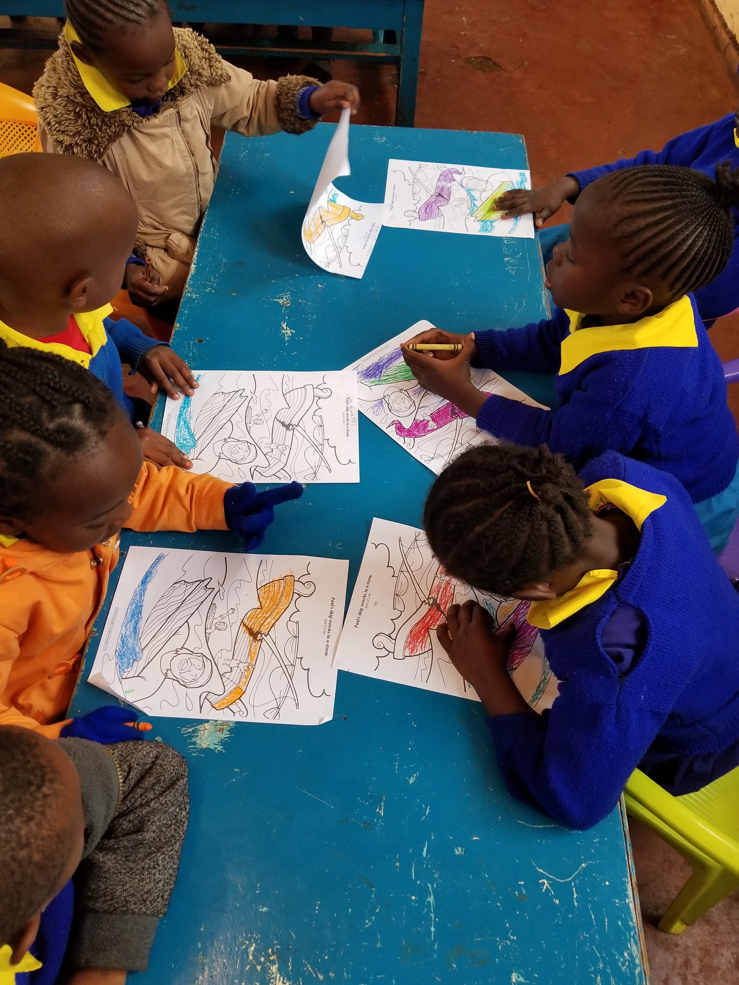 Children sitting around a blue table coloring pictures of lions and other animals.
