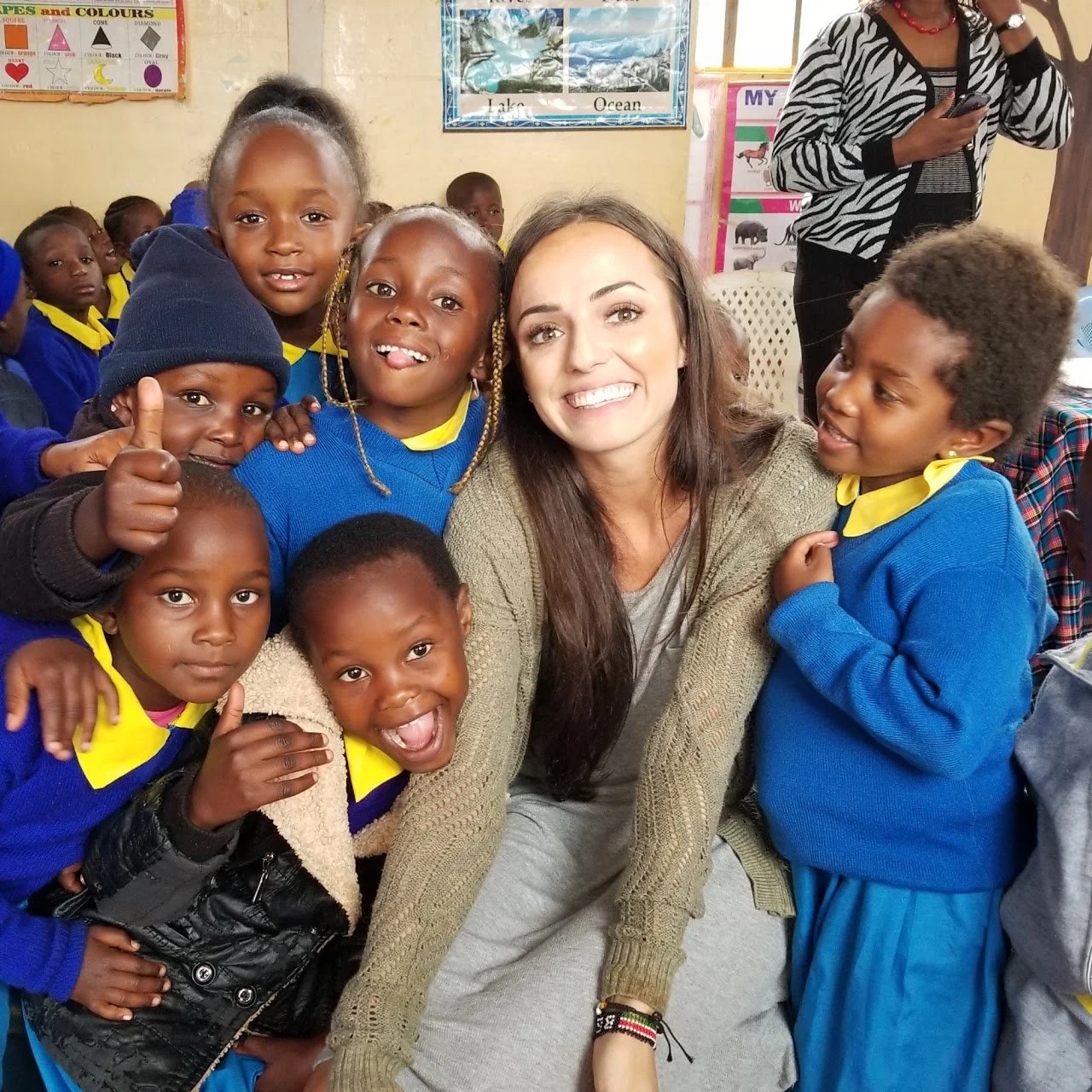 A group of young children and a woman smiling for a photo in a classroom with educational posters on the wall.