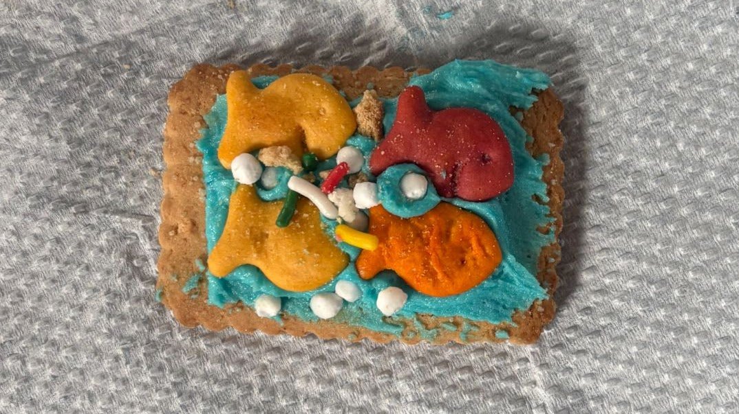 Decorated cookie with blue icing, colorful sprinkles, and small fondant decorations, on a silver textured surface.