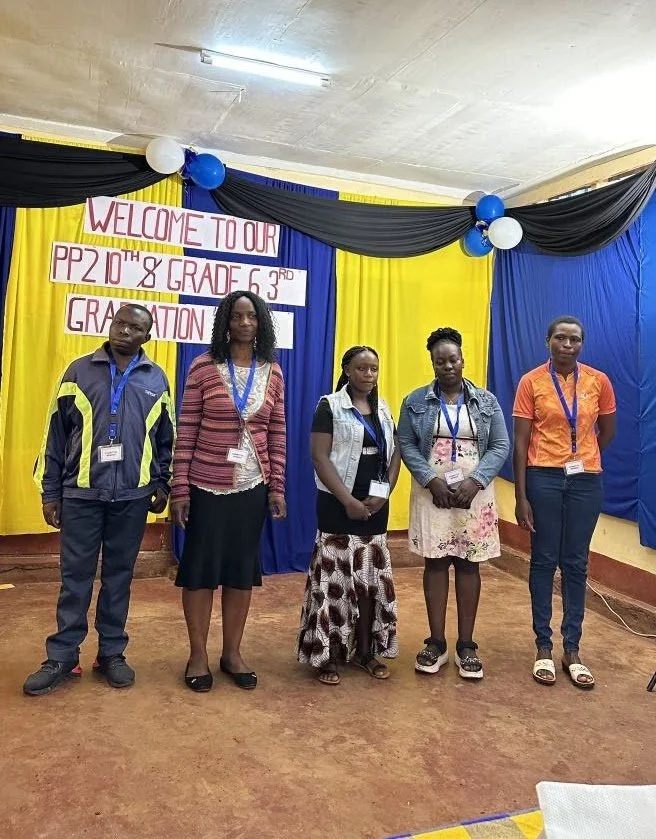Five people standing in a room with a yellow and blue backdrop and a sign that reads "Welcome to our PP2 10th & 8th Grade 6th Graduation".