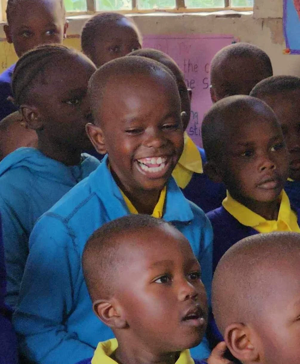 Group of smiling children in a classroom, wearing blue and yellow uniforms.