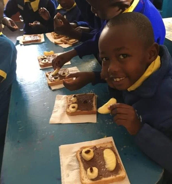 Children in school uniforms making and eating animal-shaped cookies with chocolate and vanilla filling at a blue table.