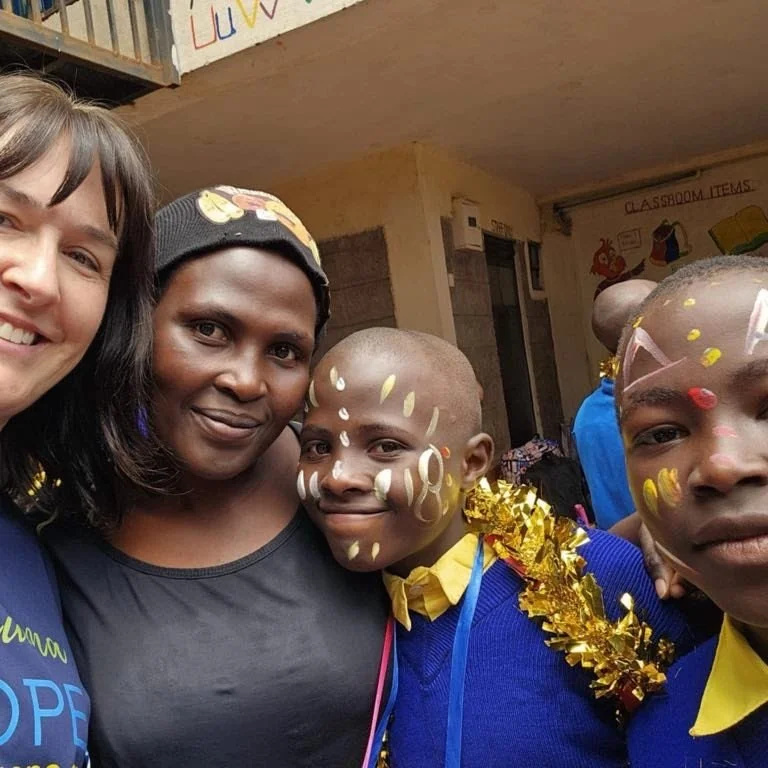 Two women and two children with face paint, wearing festive costumes, taking a group photo indoors.