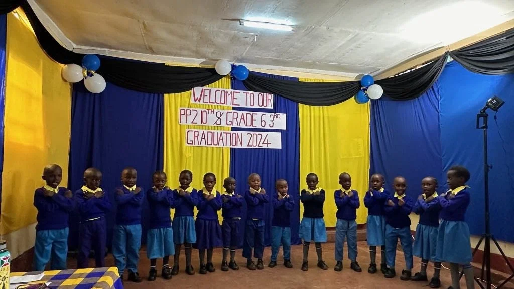 Eleven young students dressed in blue uniforms standing in a line on stage with a yellow and blue backdrop, celebrating a graduation event in 2024.