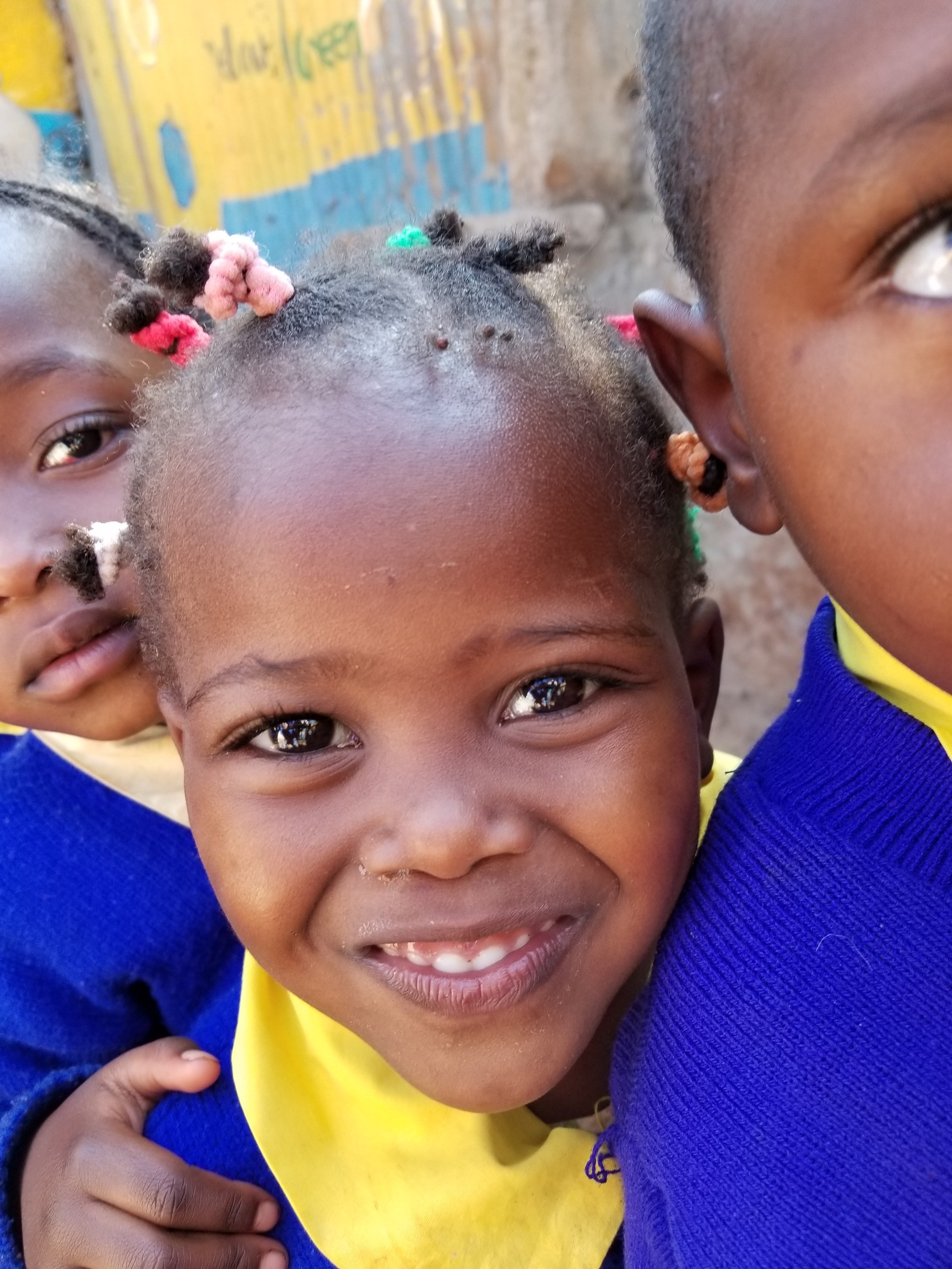 Close-up of smiling African children, wearing colorful clothing, standing outdoors.