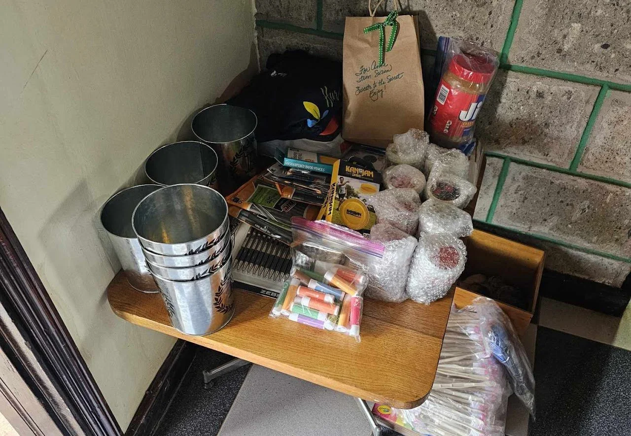 Table with various items such as aluminum cans, bubble-wrapped objects, a bag of marshmallows, a packet of sugar, and other miscellaneous supplies.