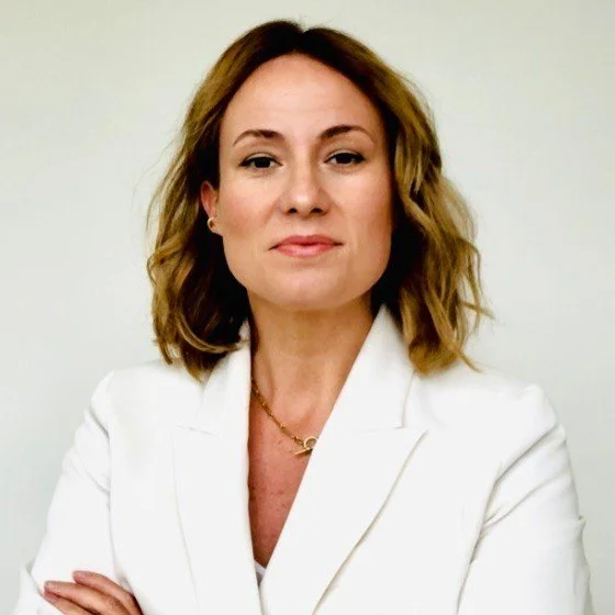 Porträt einer Frau, Swantje Ronge, mit Schulterlänge, braunen Haaren, weißem Blazer, vor einem weißen Hintergrund.