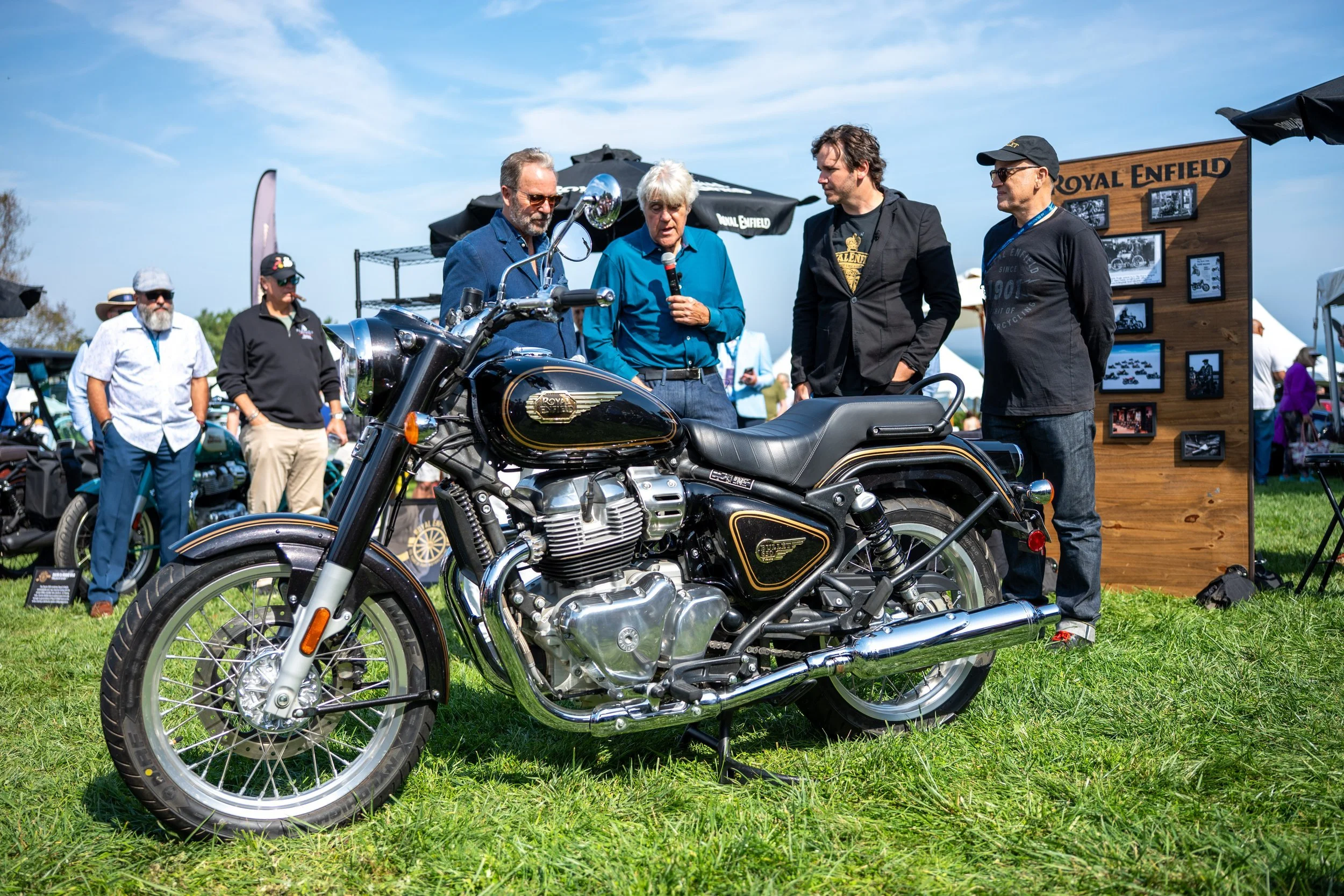 Jay Leno and guests beside a Royal Enfield motorcycle on the lawn at Audrain