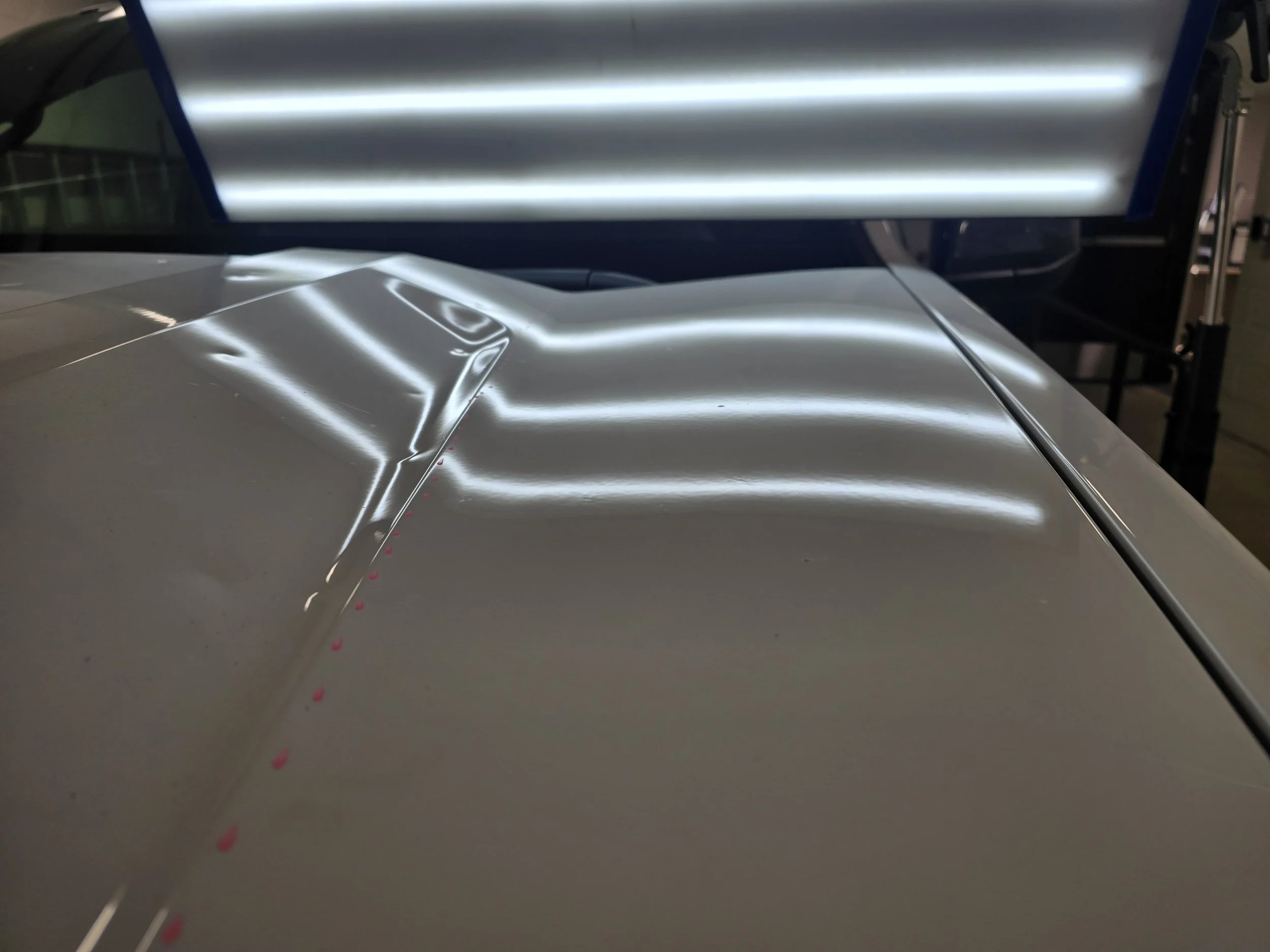 The hood of a vehicle showing hail damage is gone under a hail light. This is the after the damage was removed by a National Hail and Dent Removal PDR technician fixes the damage using non-invasive techniques.