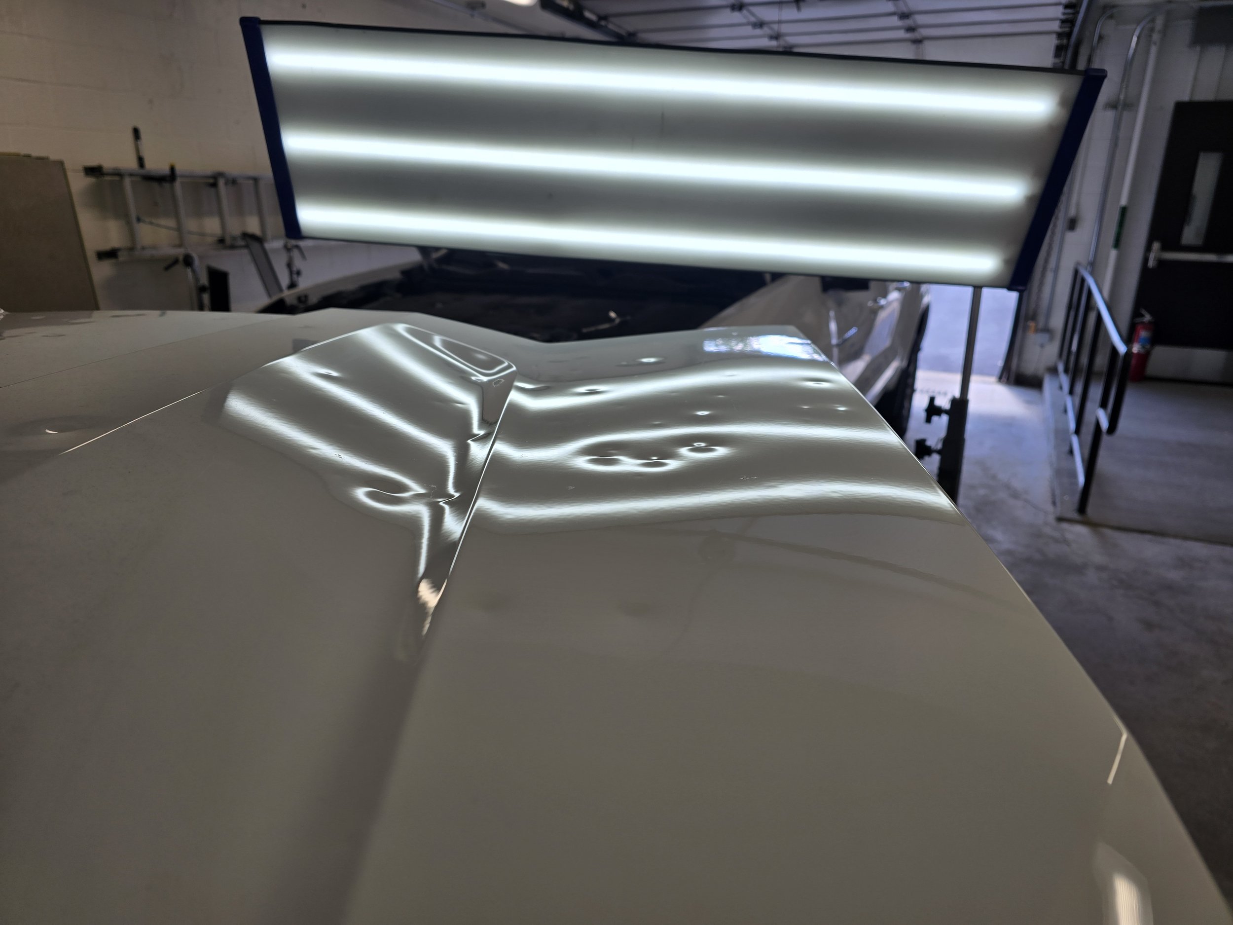 The hood of a vehicle showing hail damage under a hail light. This is the damage before a National Hail and Dent Removal PDR technician fixes the damage using non-invasive techniques.